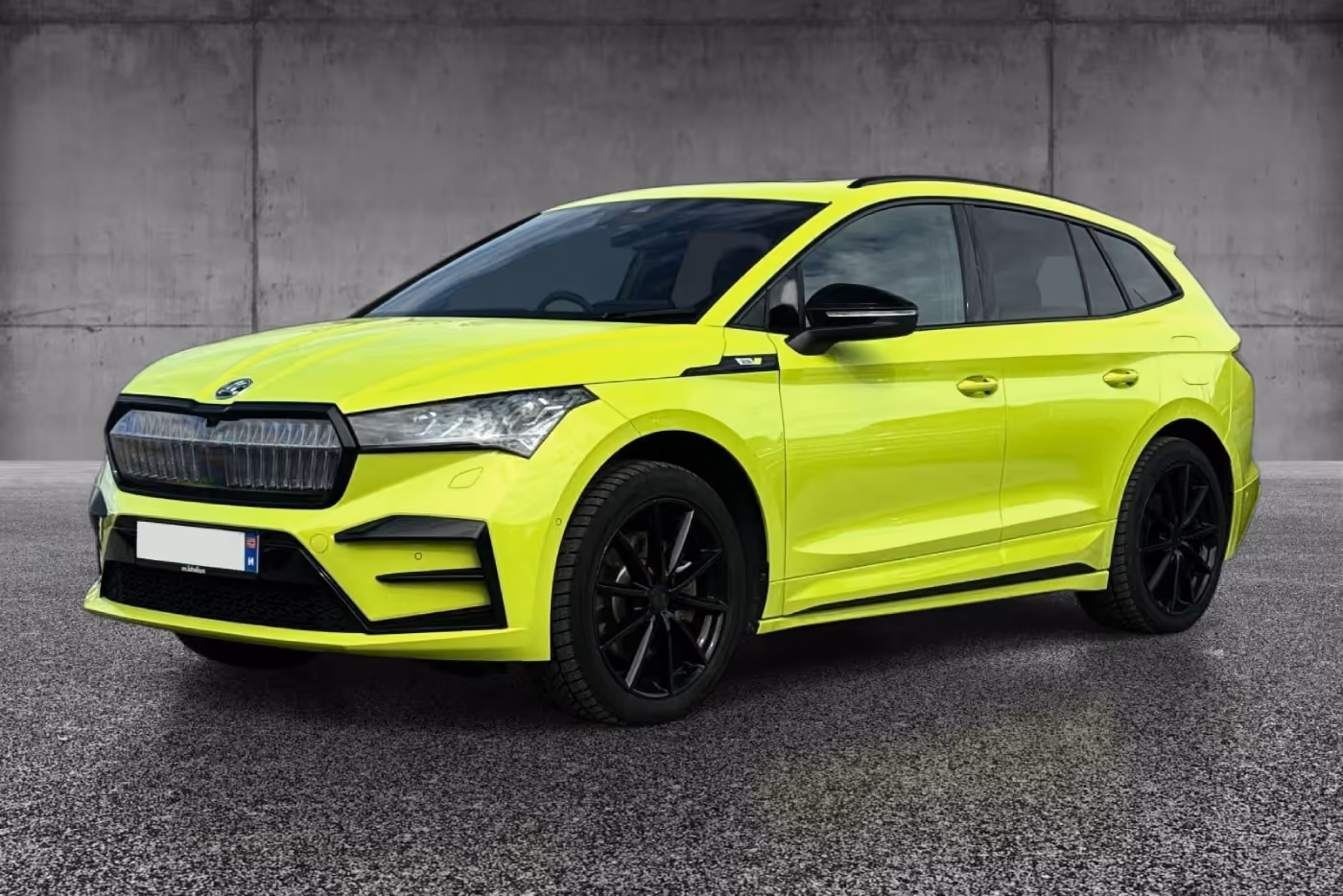 Bright yellow compact SUV with black rims parked on textured pavement against a gray concrete wall.