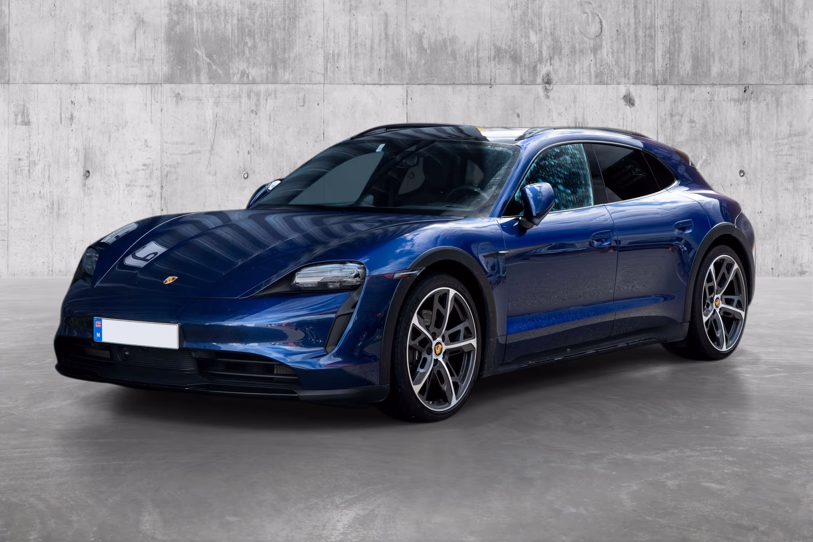 Blue Porsche Taycan Cross Turismo parked indoors against a concrete wall.