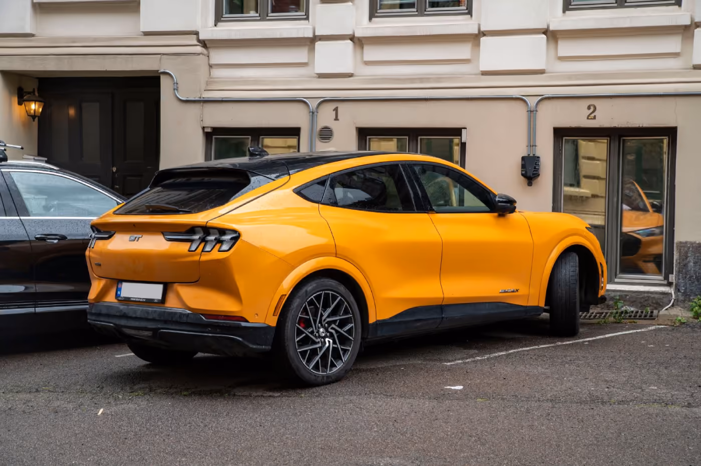 Orange Ford Mustang Mach-E GT electric SUV parked in front of a beige building with windows numbered 1 and 2.