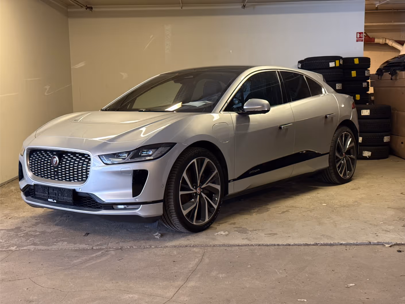Silver Jaguar I-PACE electric SUV parked indoors next to stacked tires.