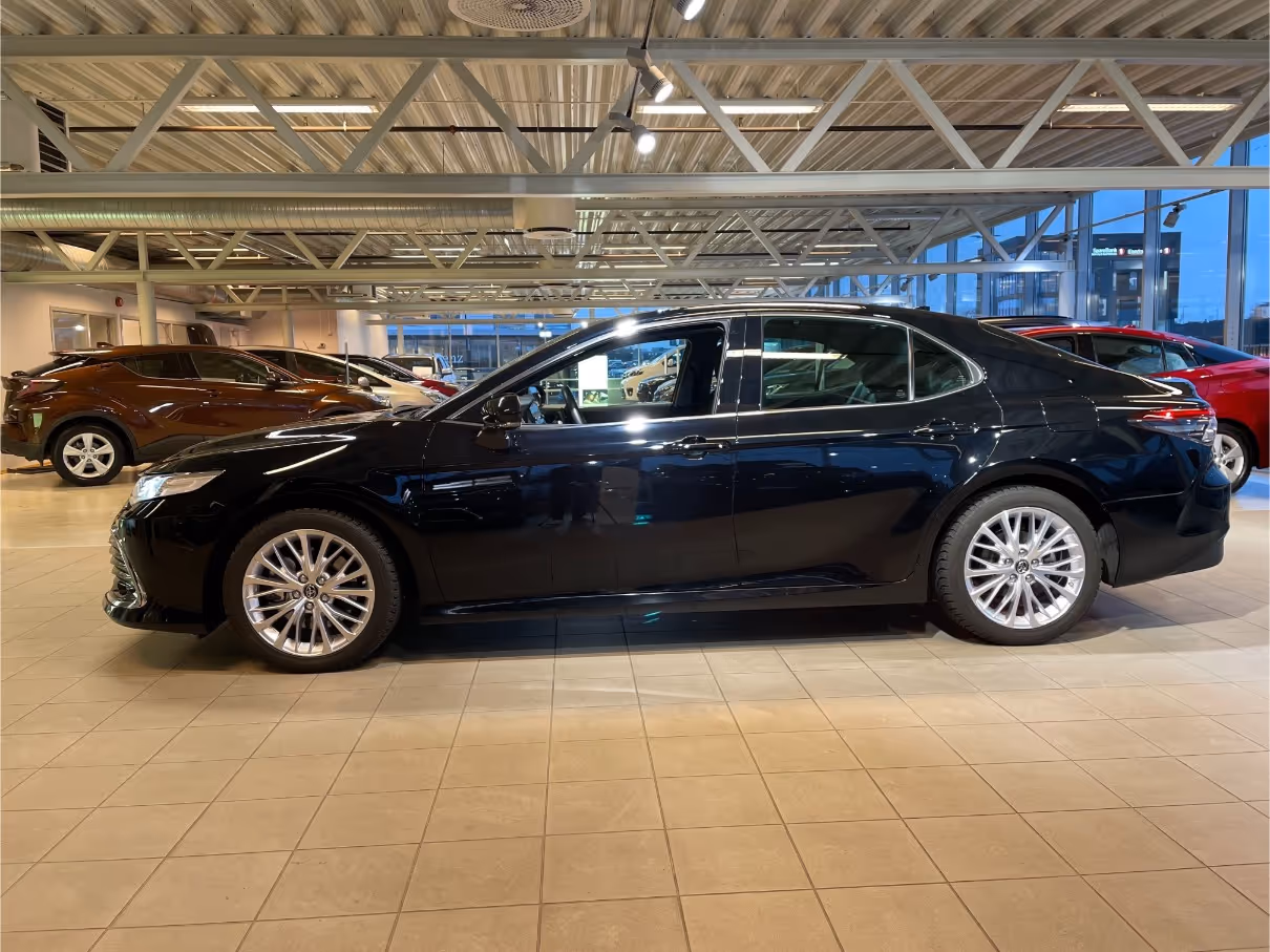 Side view of a black sedan parked inside a brightly lit car showroom with other vehicles in the background.