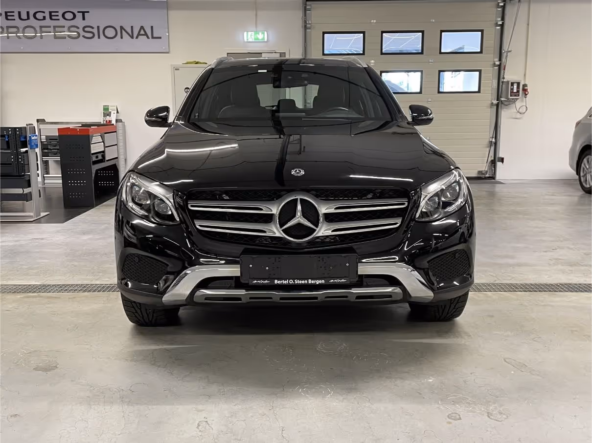 Front view of a black Mercedes-Benz SUV parked indoors with a Peugeot Professional sign in the background.