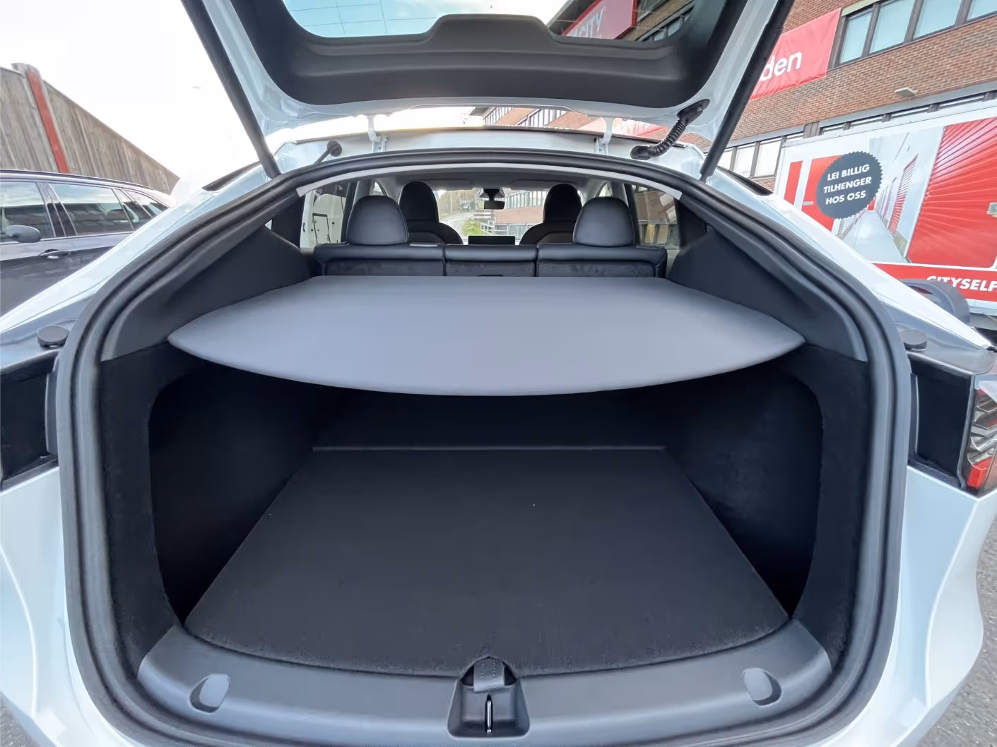 Open trunk of a white car with a retractable cargo cover and back seats visible.