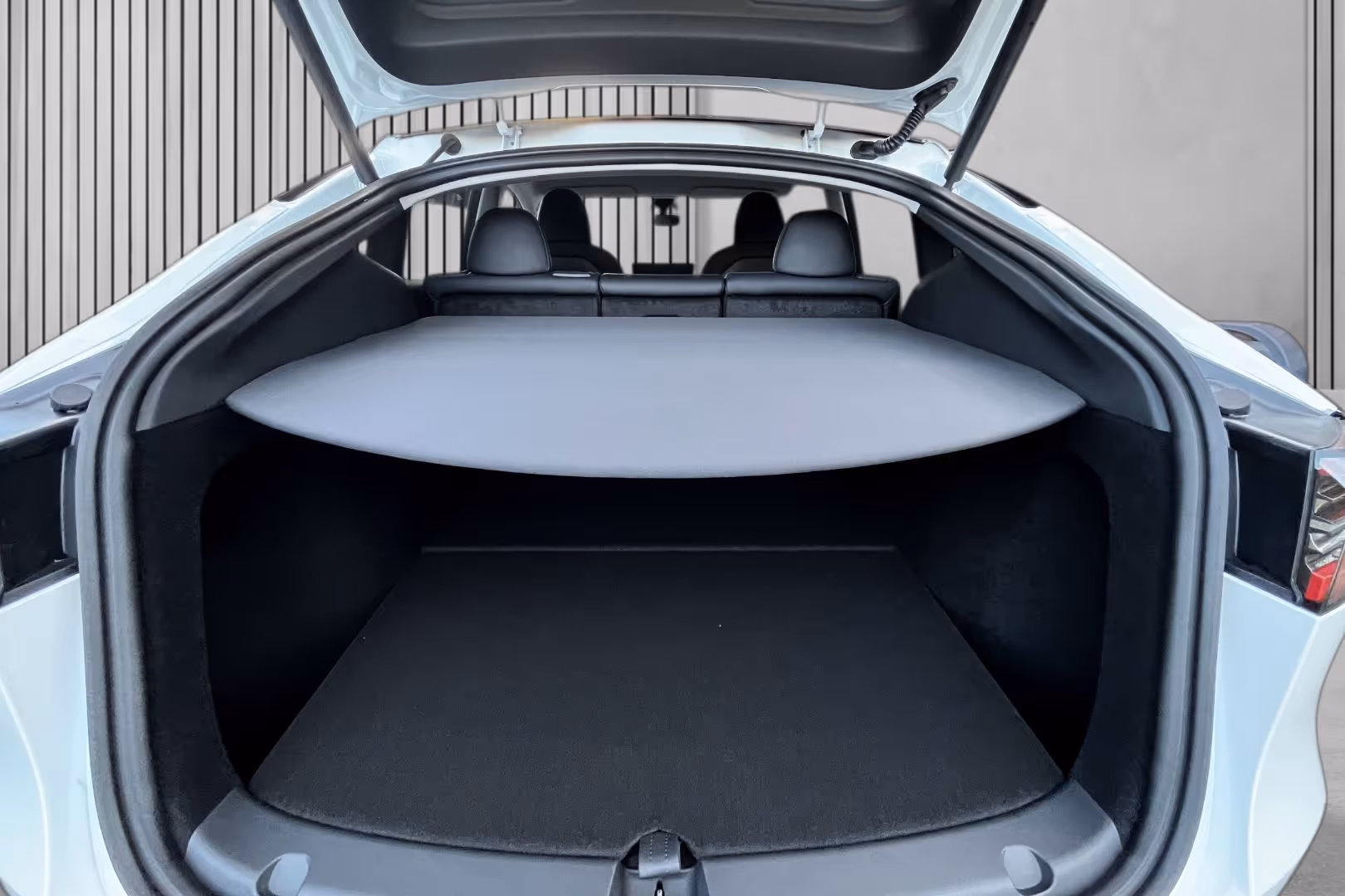 Open rear trunk area of a white electric car showing black interior with a retractable cover over the cargo space.