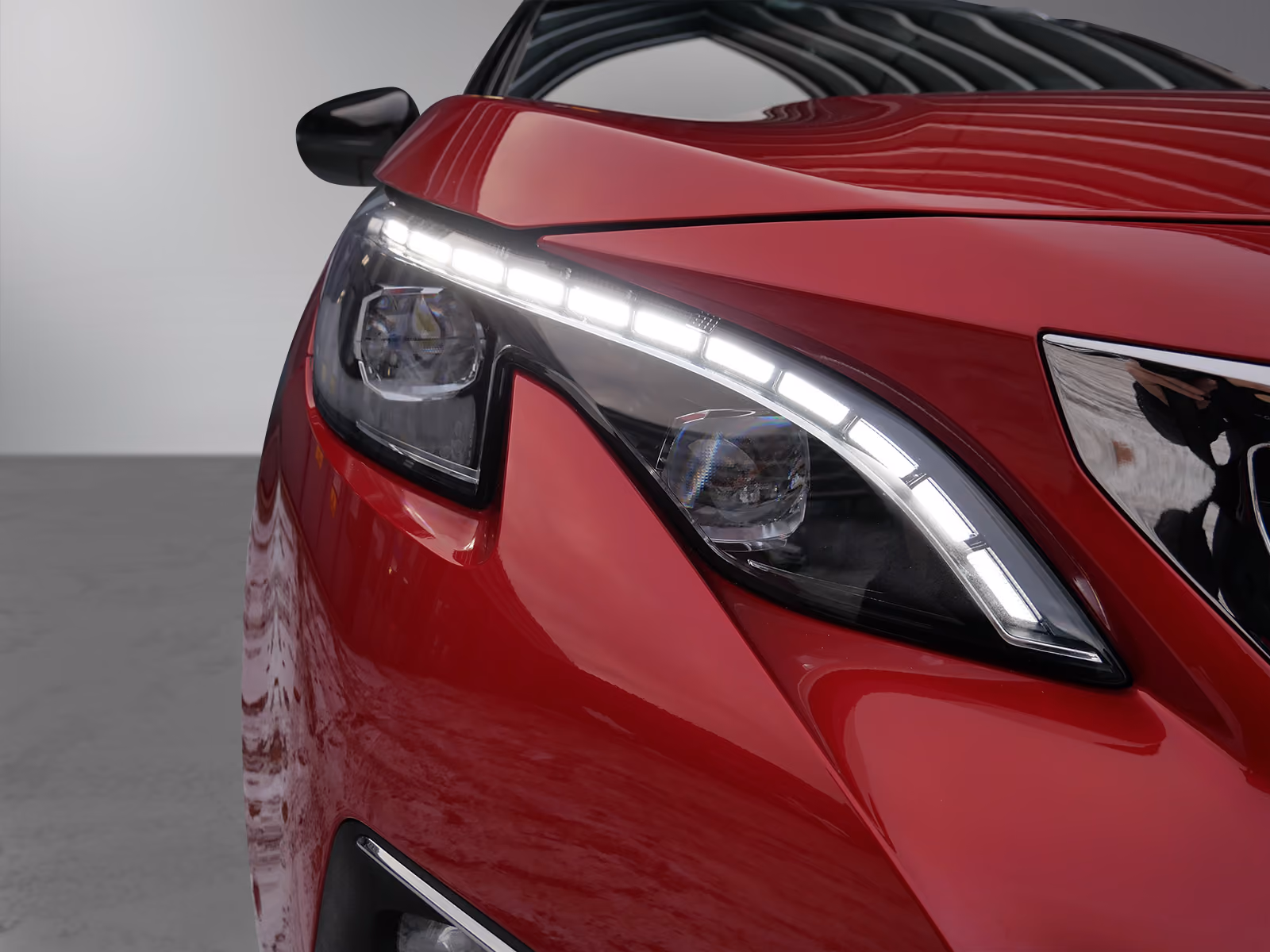 Close-up of a red car's sleek front headlight with LED daytime running lights and reflective details.