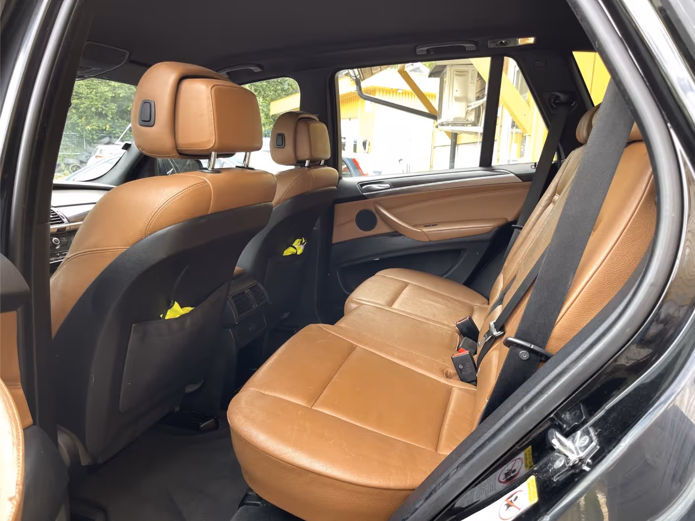 Rear interior of a car with tan leather seats and black seatbelts.