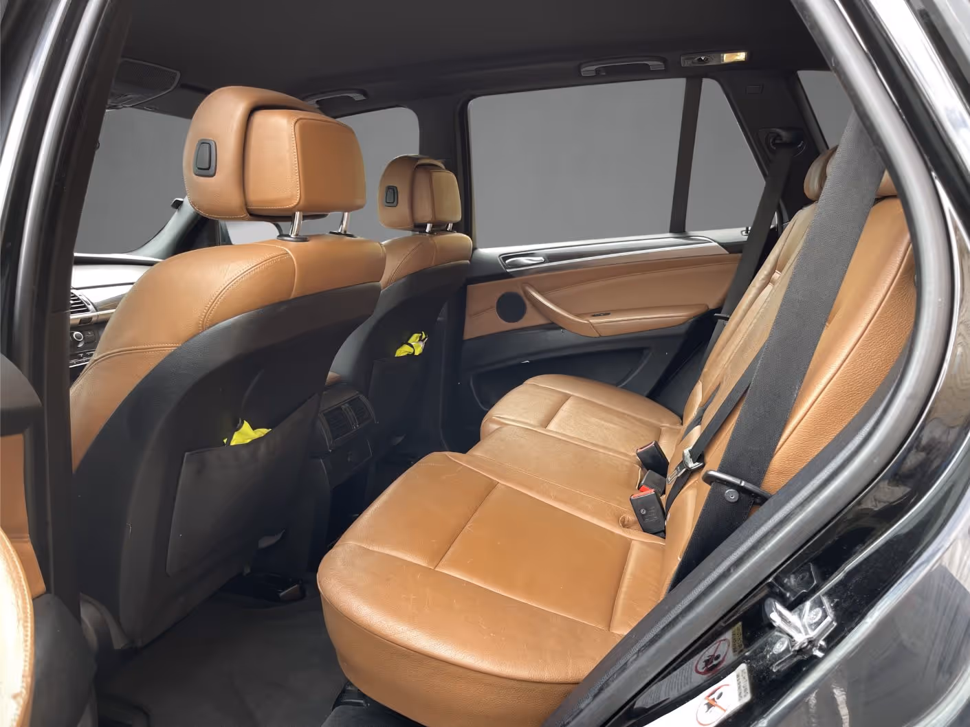 Rear passenger seats of a car with tan leather upholstery and black seat belts, viewed from the open door on the right side.