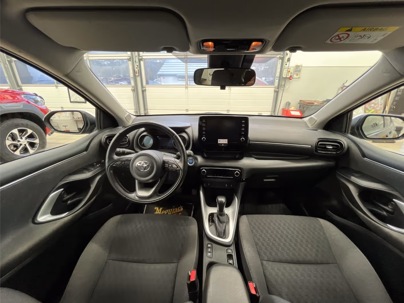 Interior view of a Toyota car showing the steering wheel, touchscreen dashboard, gear shift, and front seats.