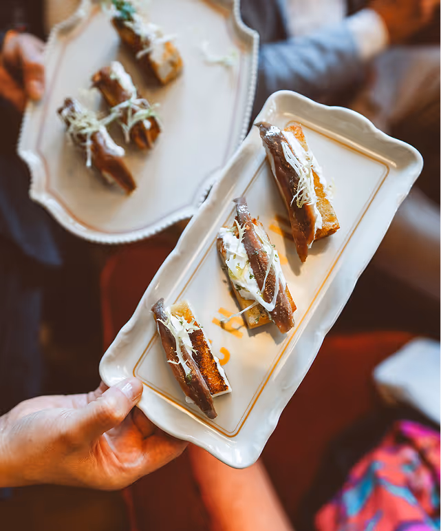 Nahaufnahme einer Vorspeise im Pellicano Restaurant Hamburg: knuspriges Brot mit Sardellenfilets, Creme und Friséesalat auf stilvollen Porzellantellern.
