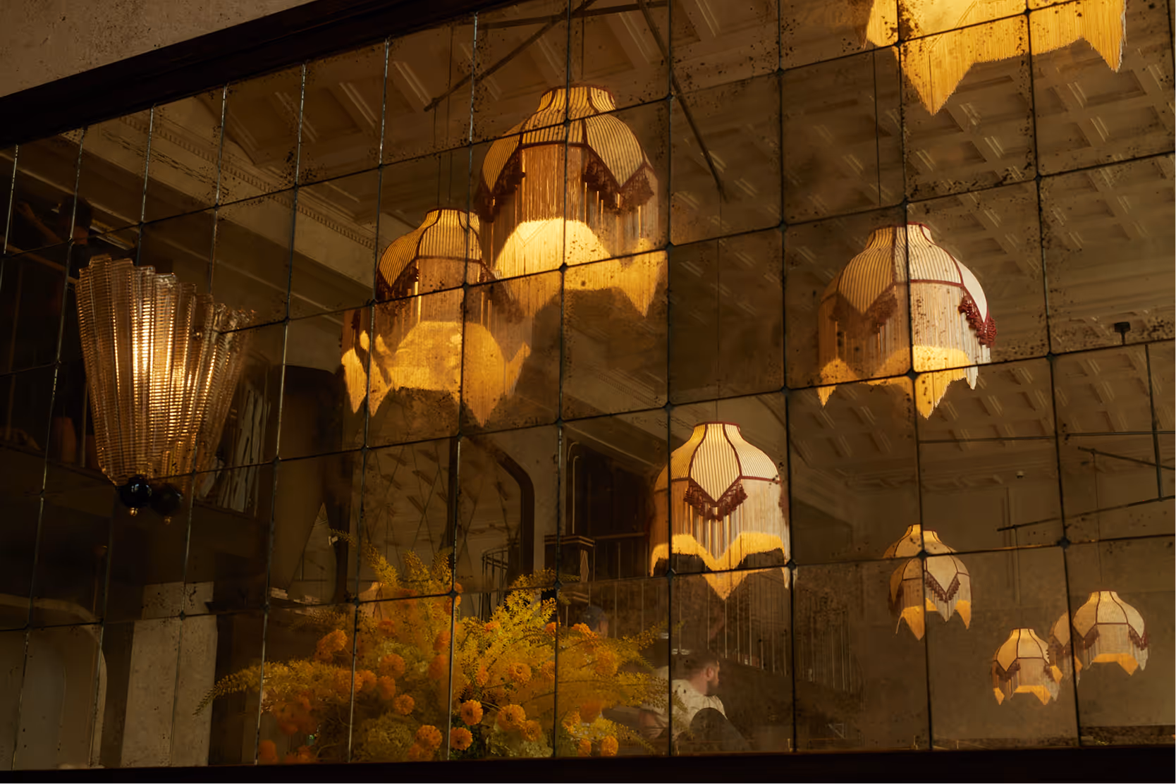 Stimmungsvolle Spiegelaufnahme im Pellicano Restaurant Hamburg – reflektierte Art-Déco-Leuchten, gelbe Blumen und architektonische Details des Innenraums.