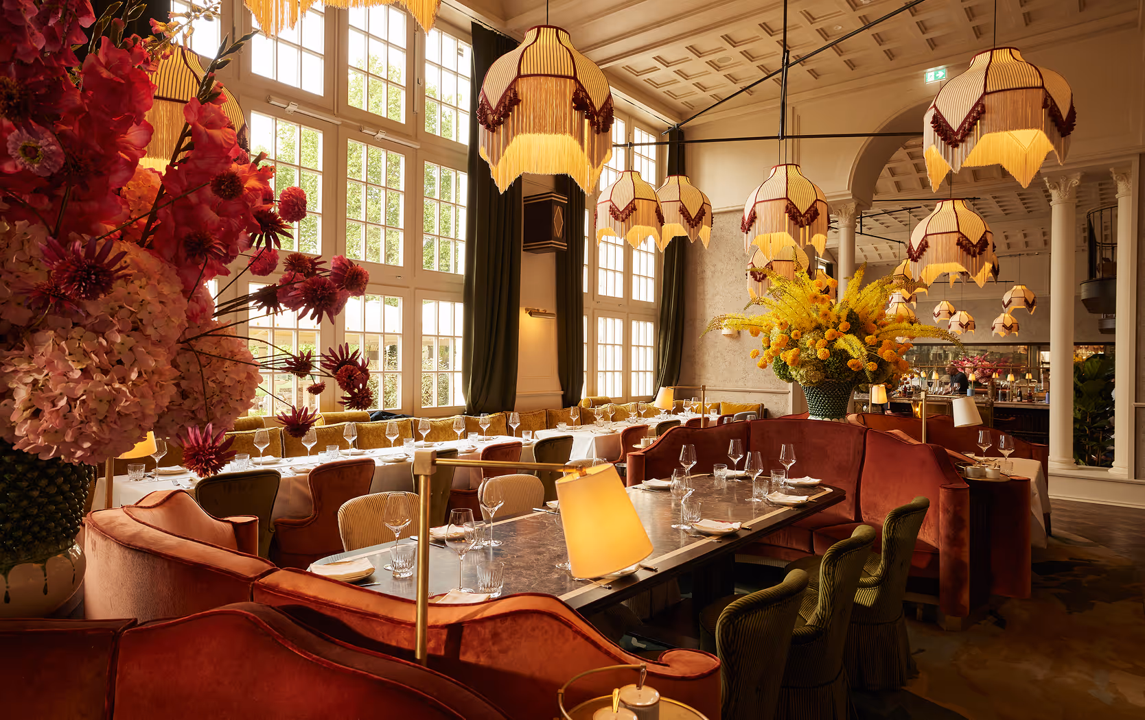 Großzügiger, lichtdurchfluteter Gastraum des Pellicano Restaurants Hamburg mit hohen Fenstern, opulenten Blumenarrangements und eleganter Art-Déco-Einrichtung.