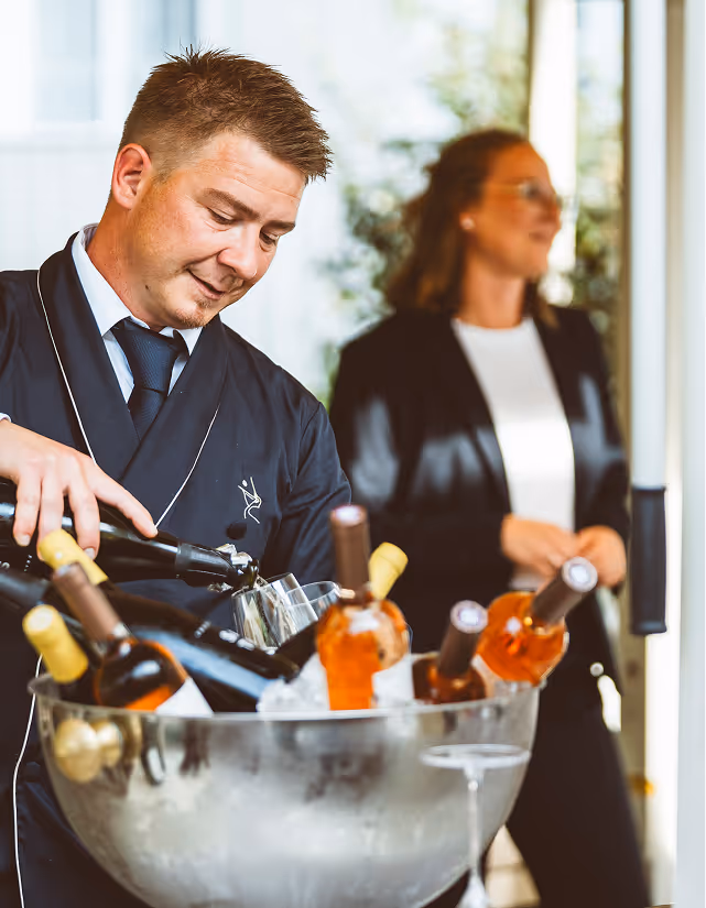 Mitarbeiter des Pellicano Restaurants Hamburg schenkt Wein aus einer mit Eis gekühlten Flasche ein – stilvoller Service bei Tageslicht.