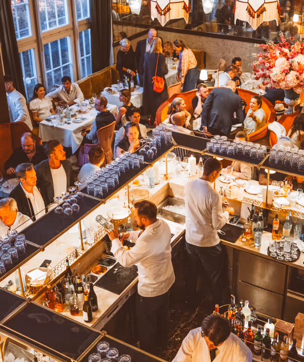 Abendstimmung im Pellicano Restaurant Hamburg: Blick von oben auf eine lebendige, elegante Restaurant- und Bar-Szene mit Gästen und Servicepersonal in stilvollem Ambiente.
