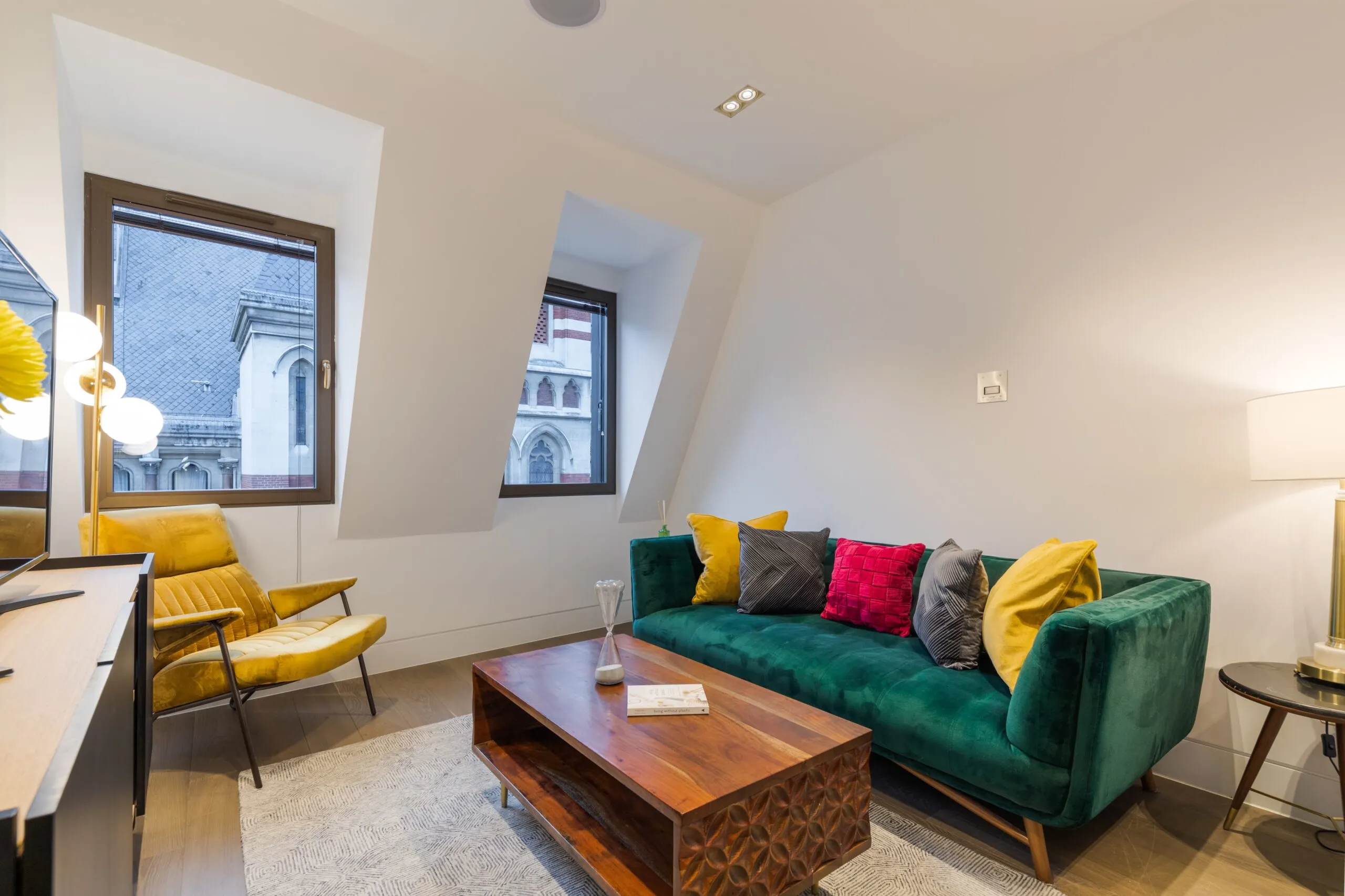 Modern living room with vibrant furniture, angled windows, and a view of historic architecture.