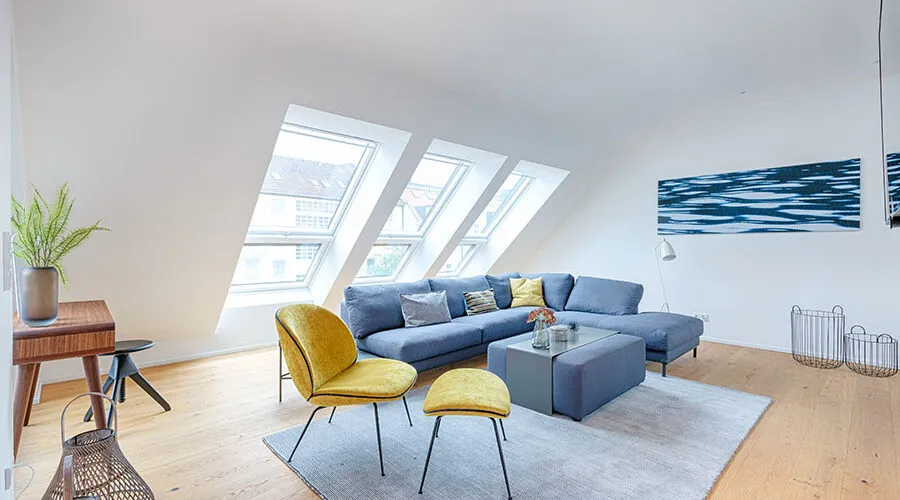 Modern living room with sloped ceiling, skylights, blue sectional sofa, and yellow accent chairs.