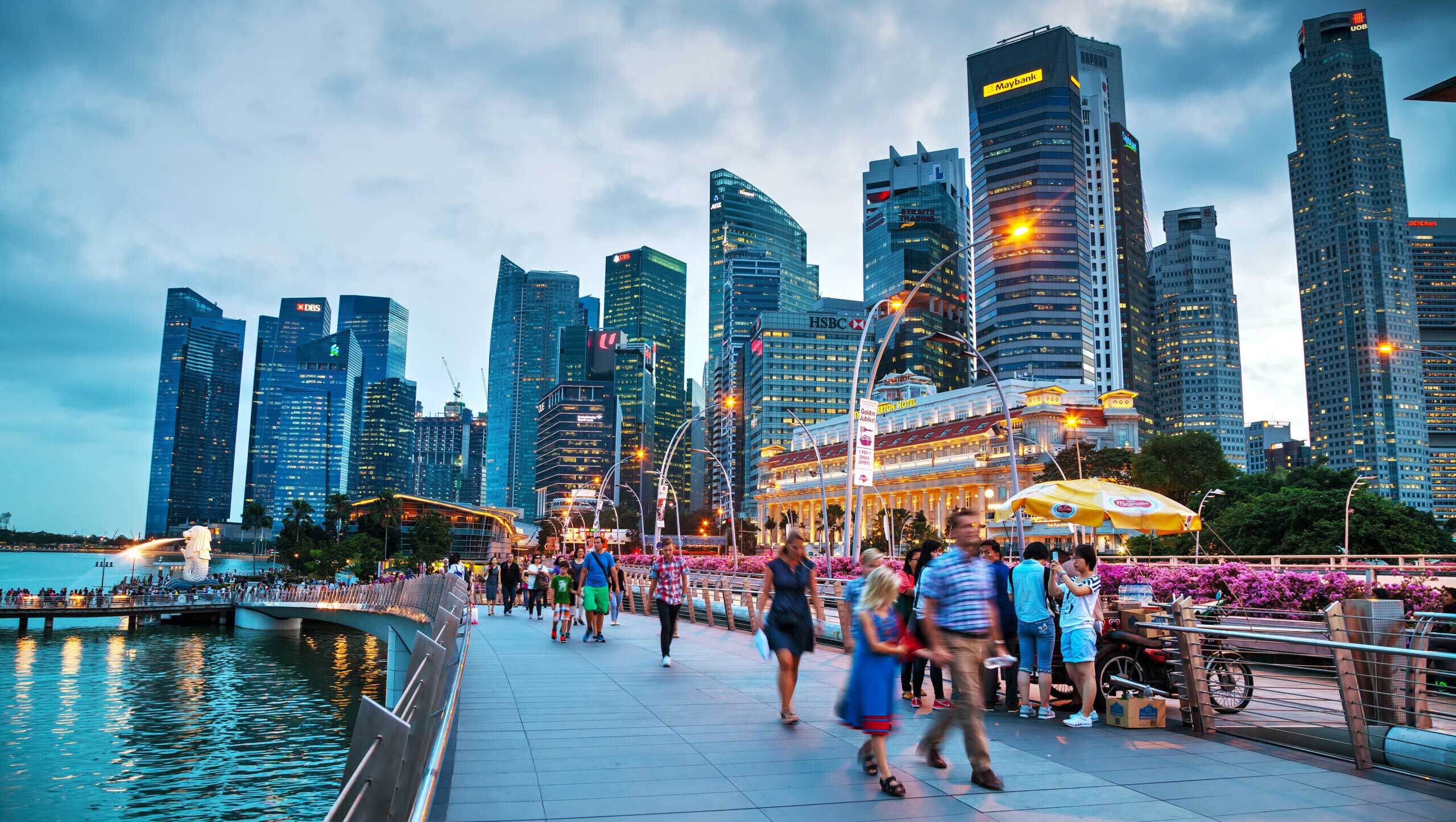 A vibrant cityscape featuring Singapore's Marina Bay skyline and the iconic Merlion statue at dusk.