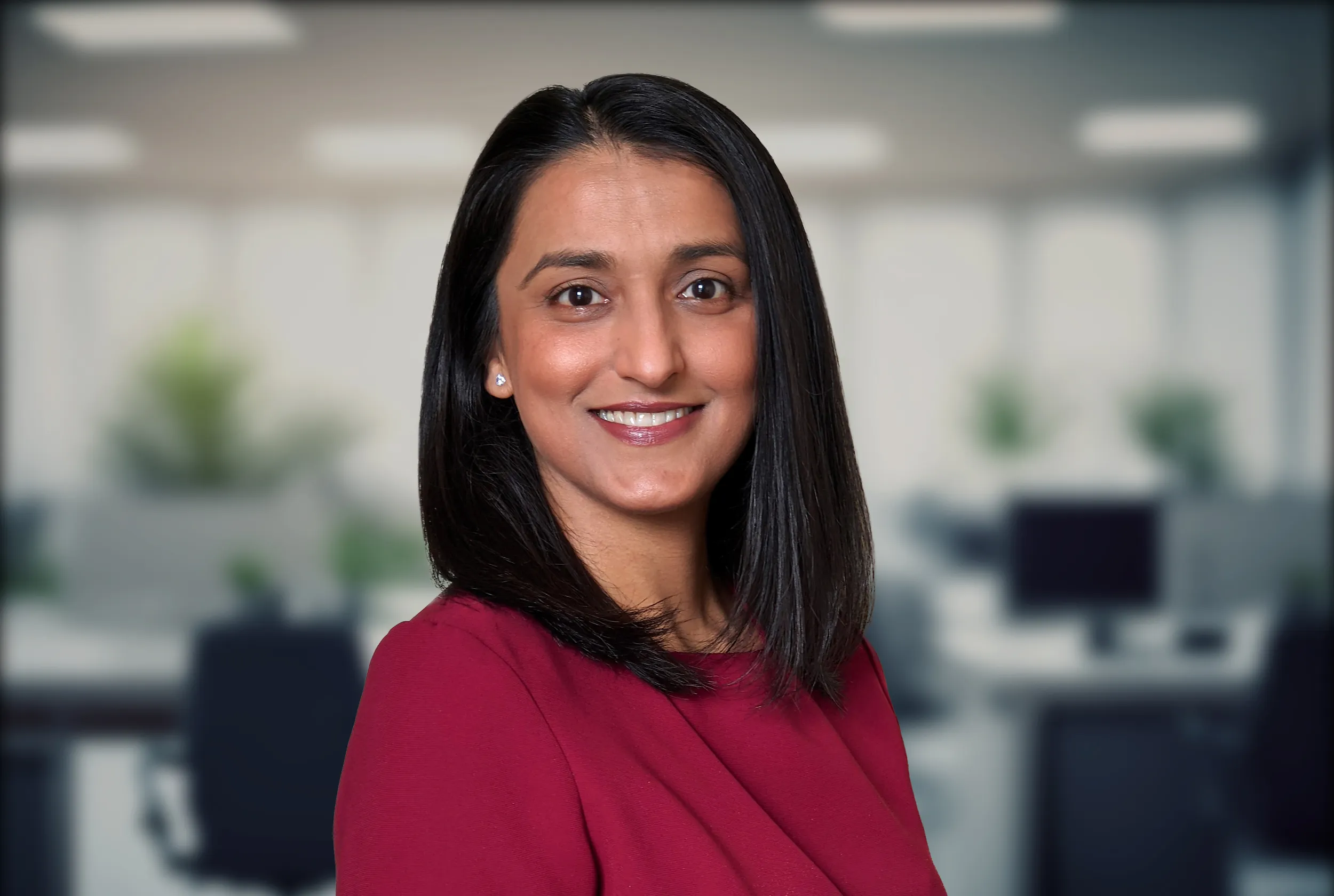 A professional setting with a woman wearing a red blouse and dark, straight shoulder-length hair.