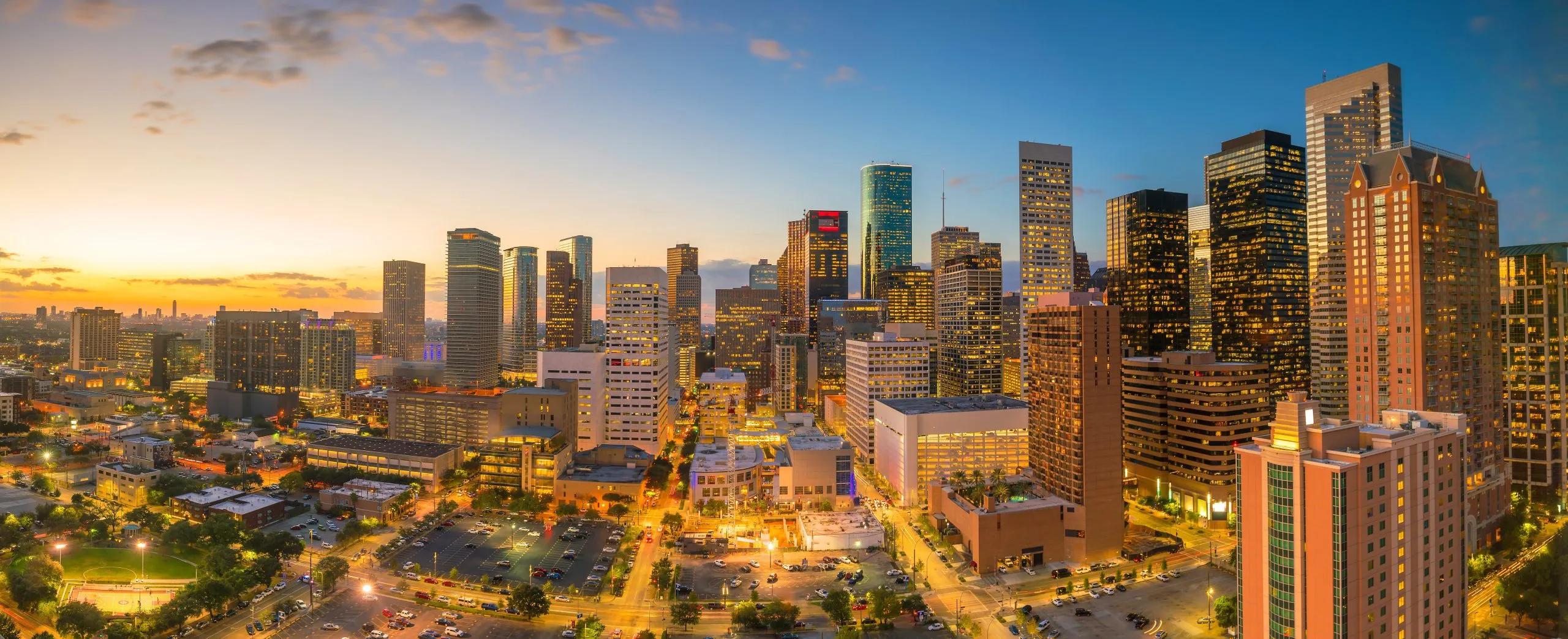 Downtown Houston skyline at sunset, featuring illuminated skyscrapers and urban streets below.