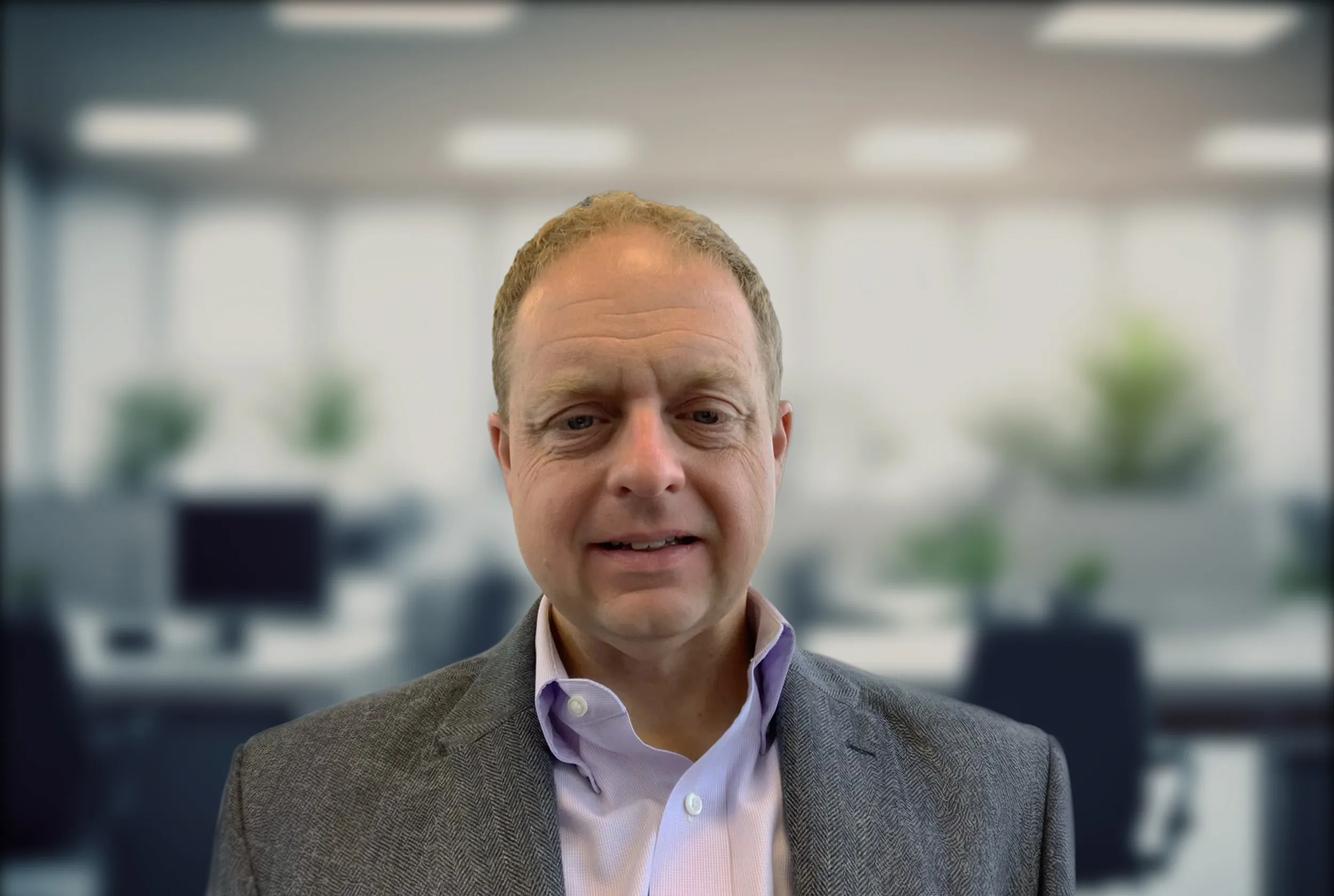 A professional office setting with a man wearing a suit jacket and collared shirt in focus.