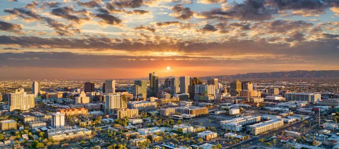 A vibrant city skyline at sunset, with scattered clouds and mountains in the background.