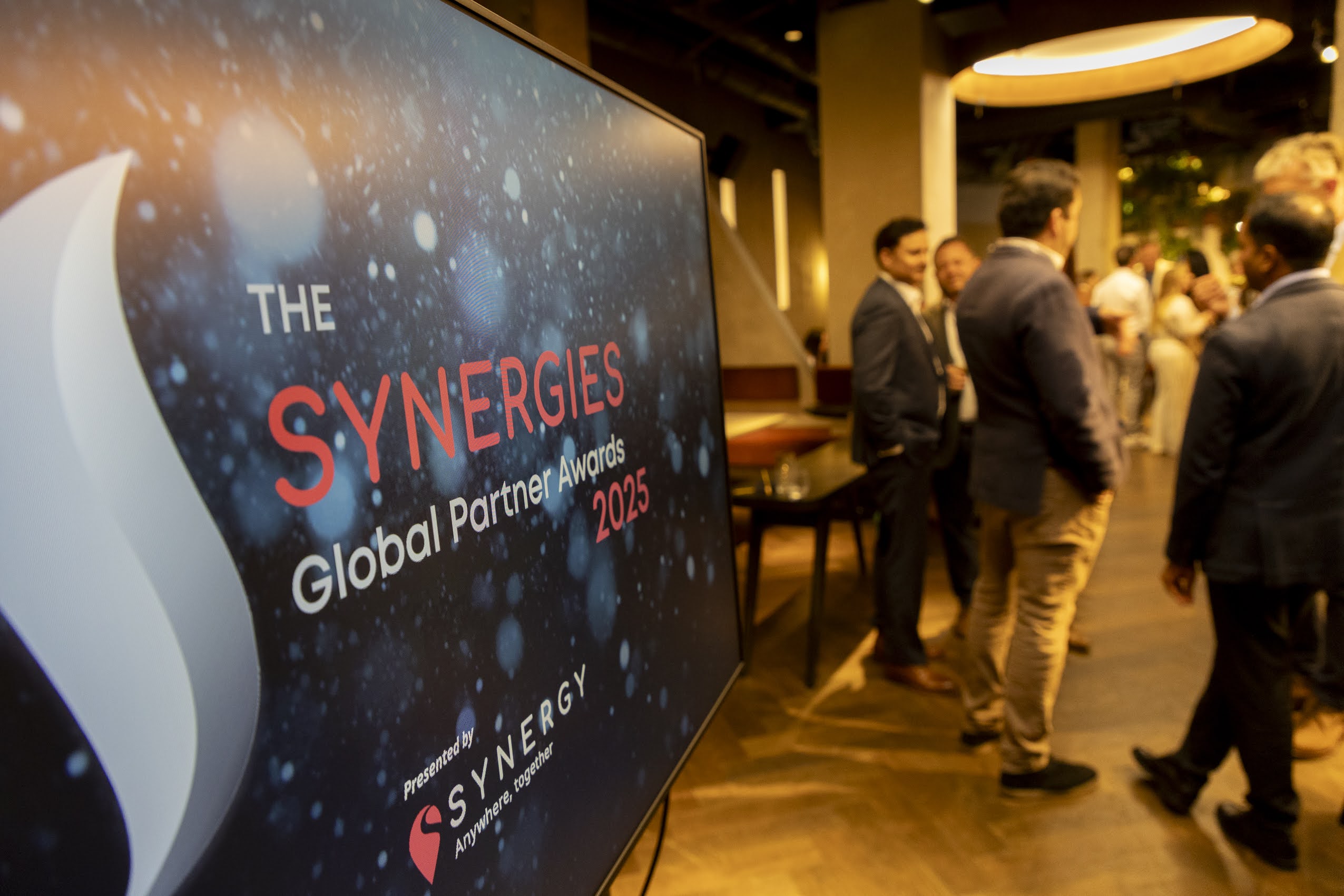 The Synergies Global Partner Awards 2025 event features attendees networking in a modern venue.