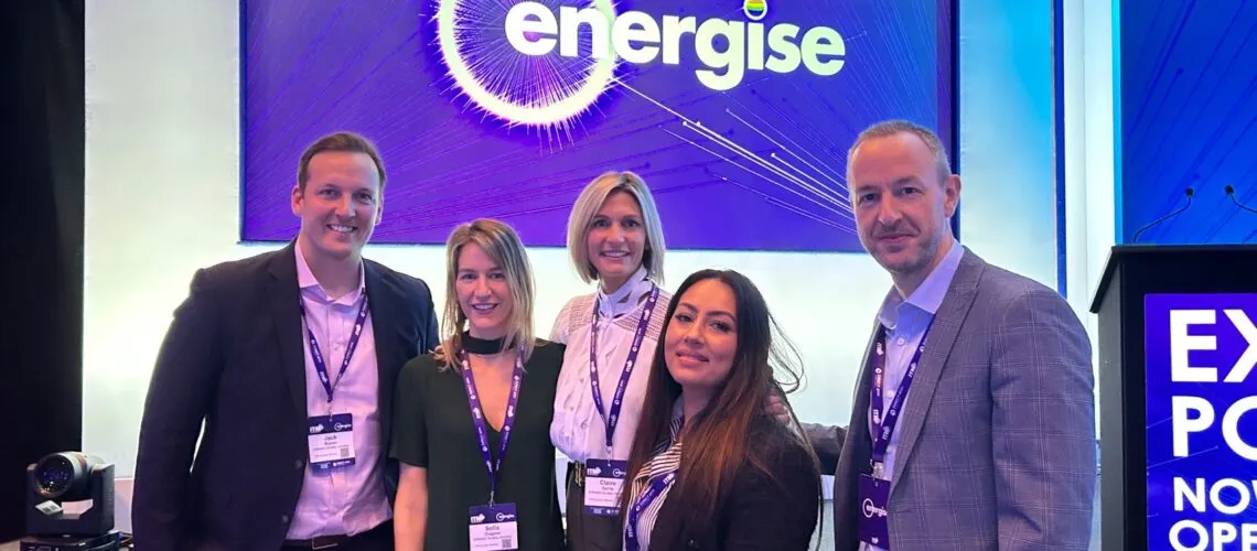A group of professionals stands at an event with "Energise" branding and conference badges visible.