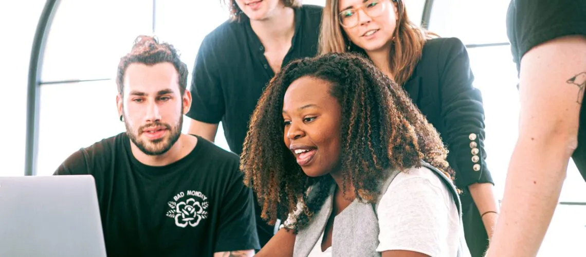 A group collaborates around a laptop in a bright, modern workspace.