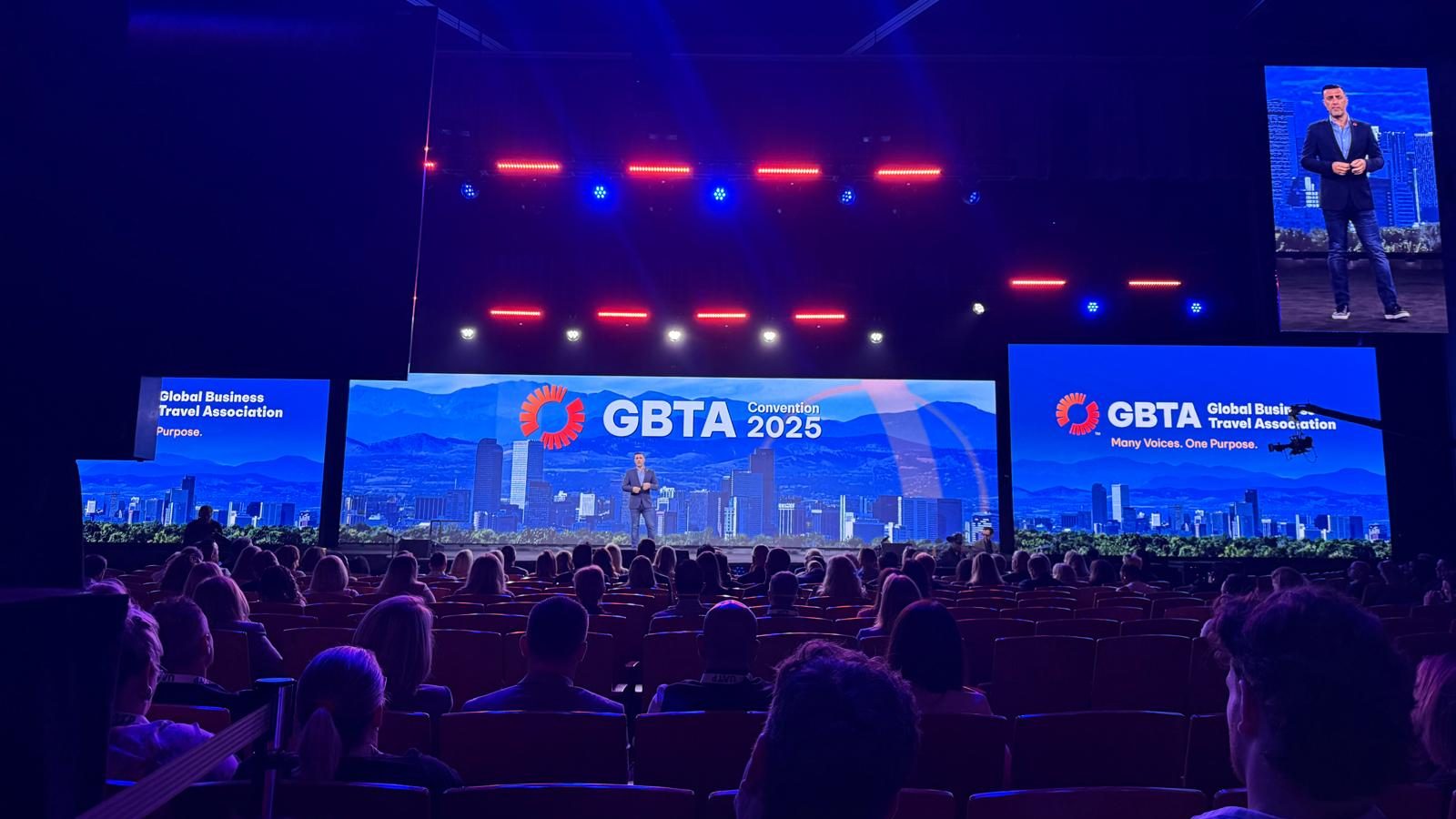 A conference stage displays "GBTA Convention 2025" with attendees seated in a large auditorium.