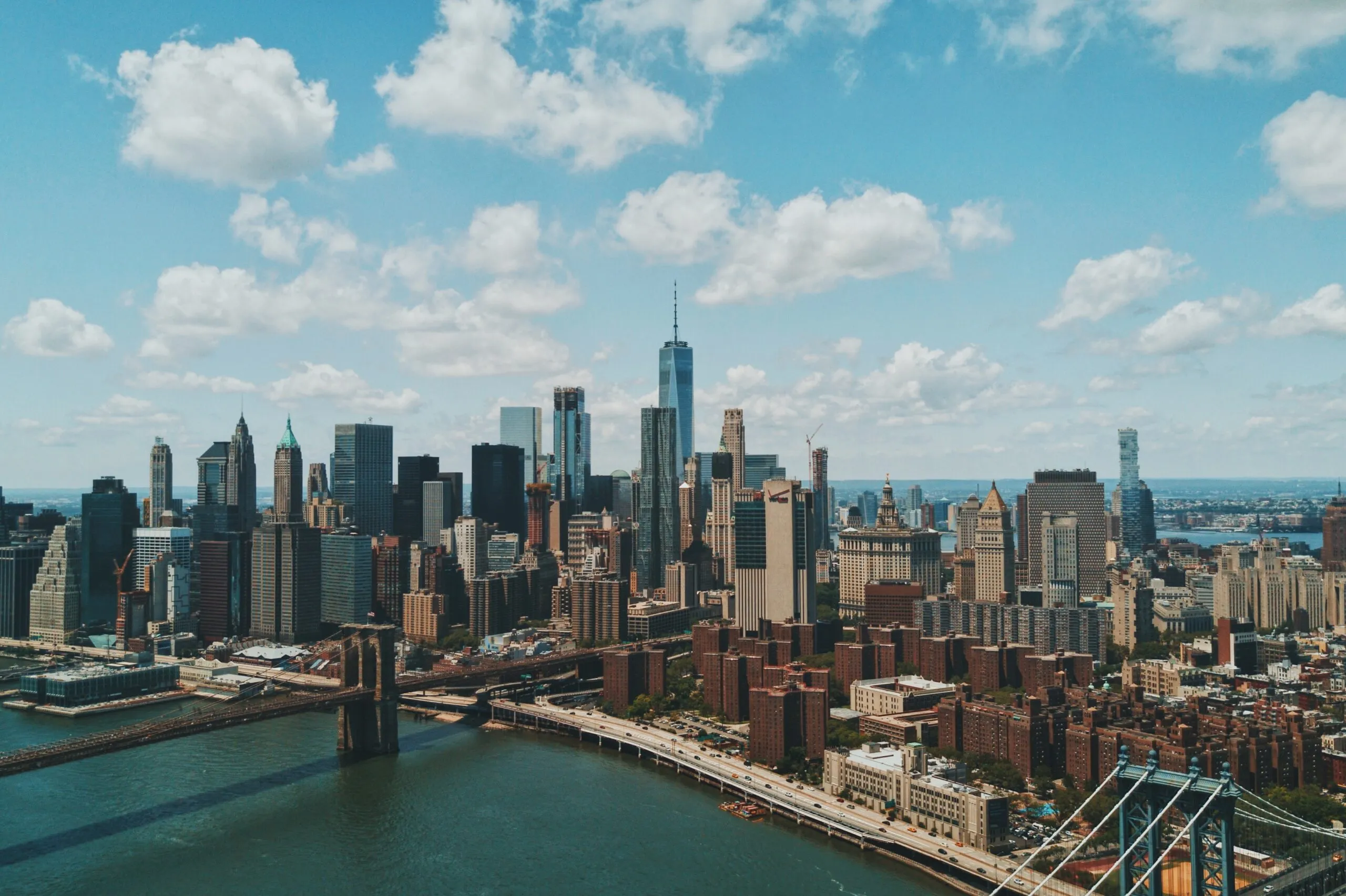 Aerial view of Manhattan skyline with skyscrapers, bridges, and the East River under a cloudy sky.