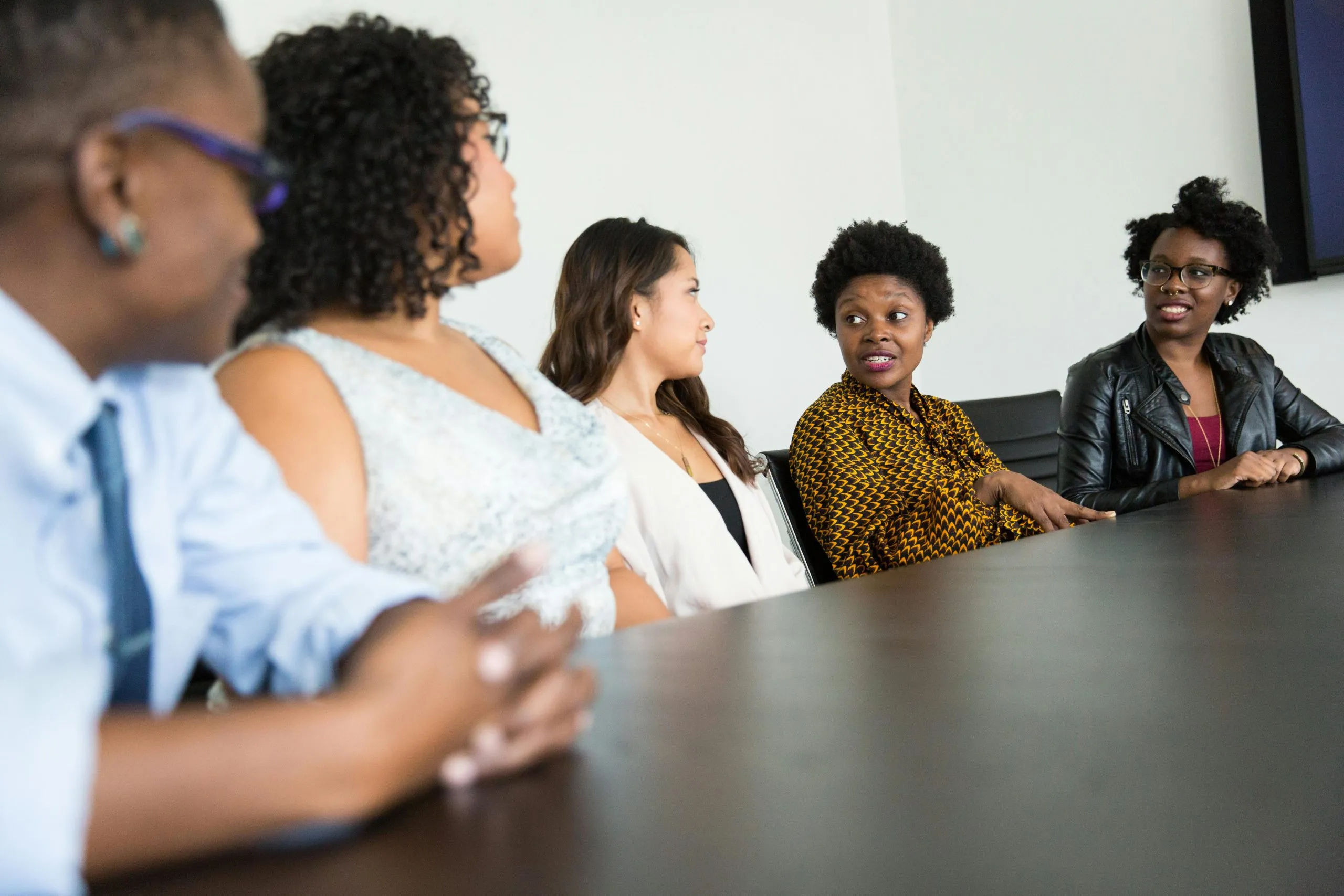 A diverse group of people sits at a conference table, engaged in a professional discussion.