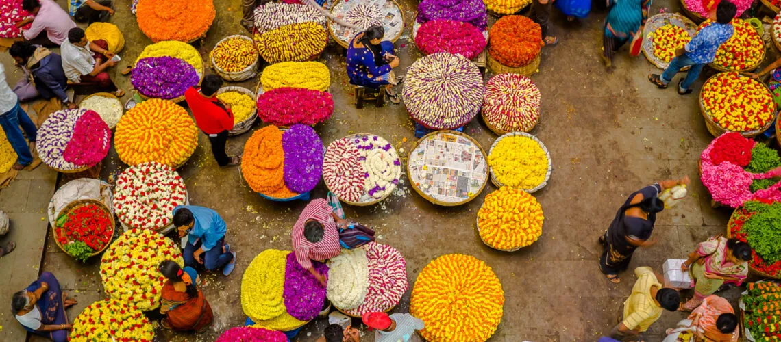 A vibrant flower market with colorful blooms in baskets, bustling with vendors and customers.