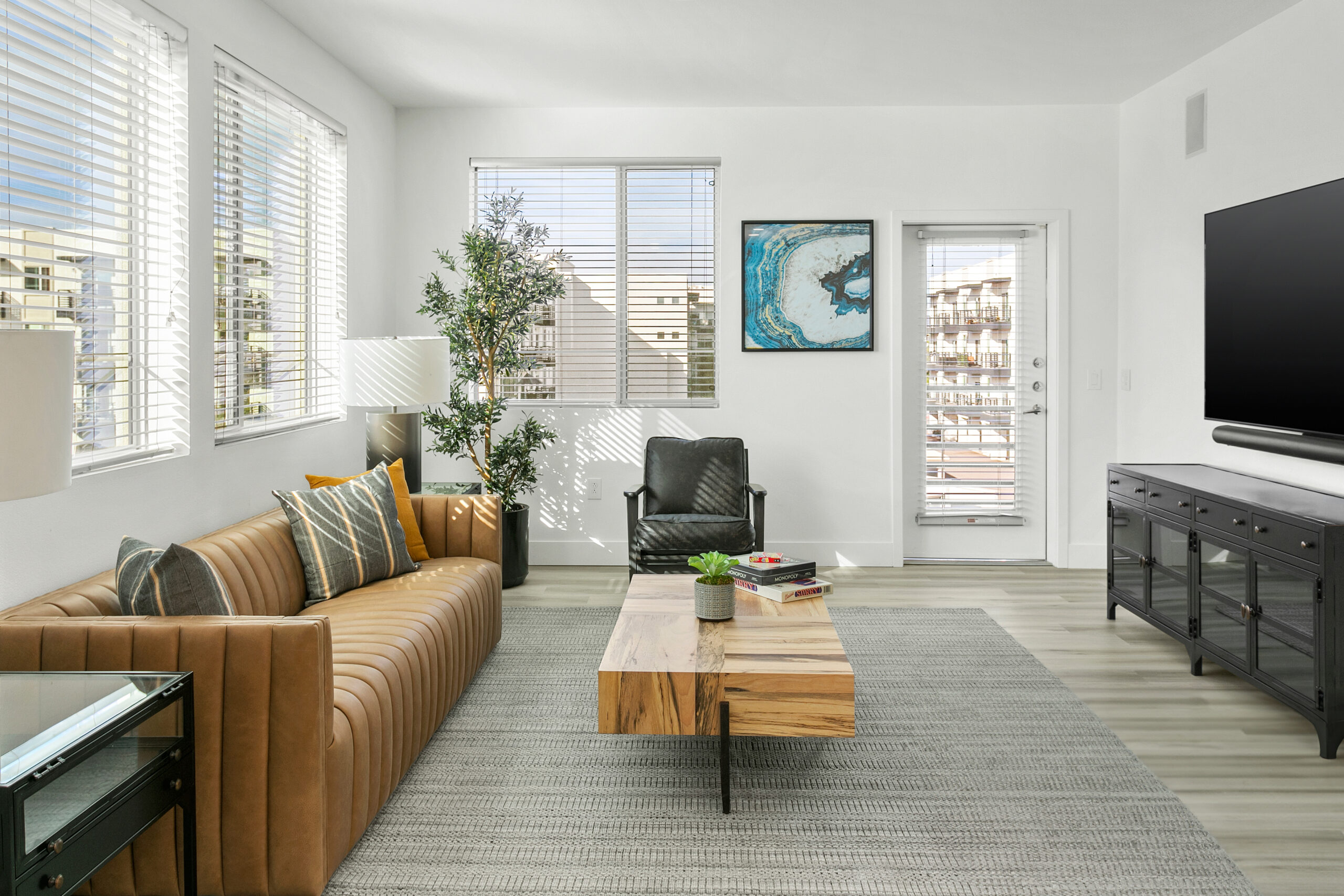 A modern living room with a leather sofa, wood table, and large windows for natural light.