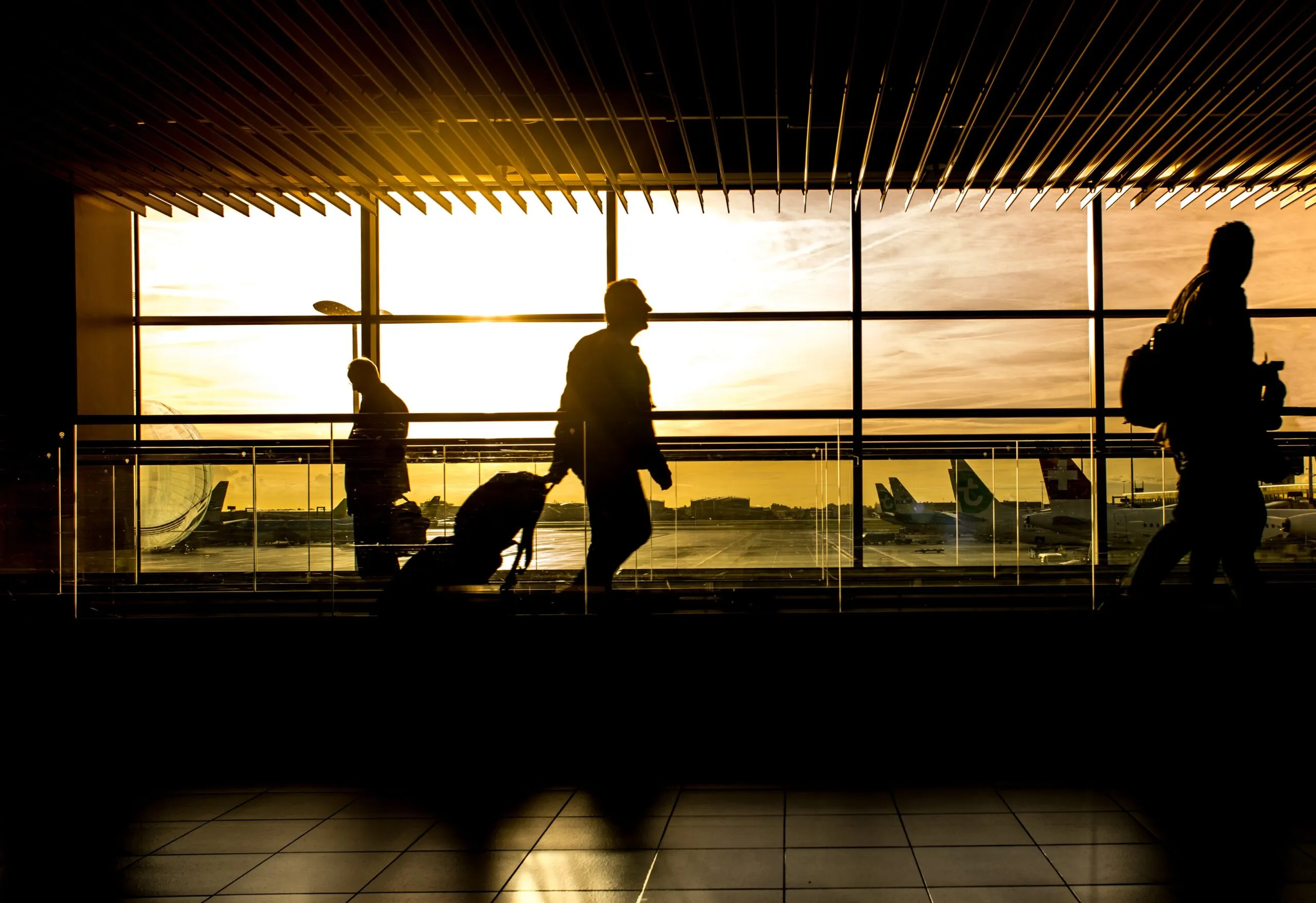 Silhouettes of travelers with luggage at an airport terminal during sunset.