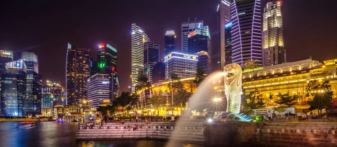 Singapore's skyline at night with the iconic Merlion statue and illuminated skyscrapers.