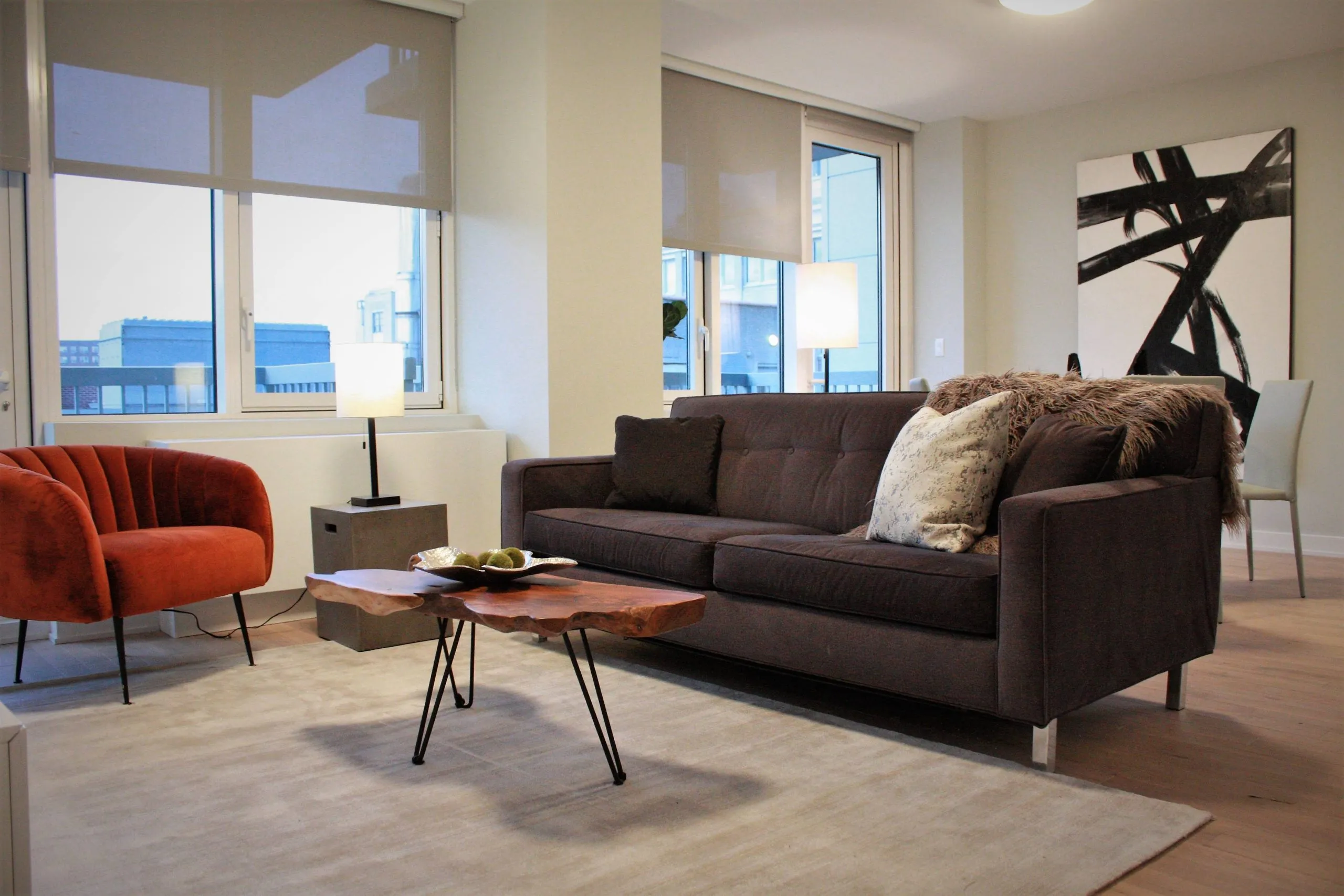 Modern living room with a brown sofa, orange chair, abstract art, and a wooden coffee table.