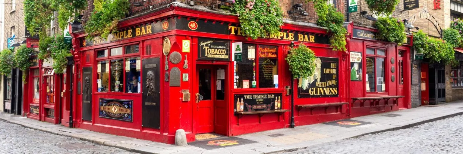 A vibrant red pub, The Temple Bar, adorned with greenery, sits on a cobblestone street corner.