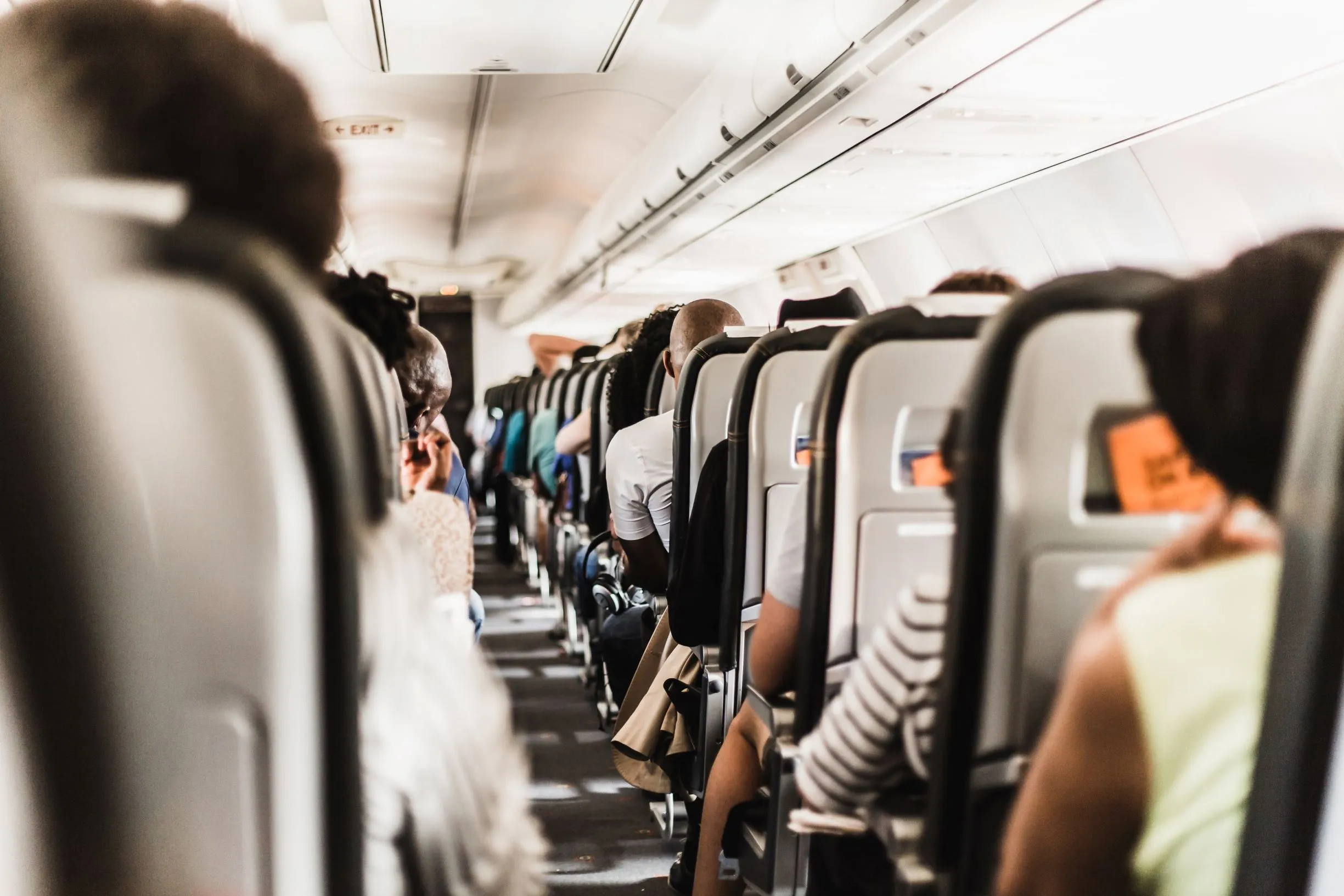 Passengers seated in rows on a commercial airplane, viewed from the aisle.