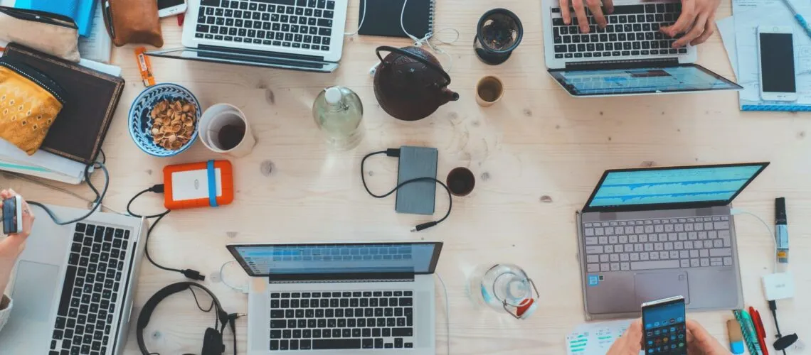 A collaborative workspace with laptops, phones, and accessories on a wooden table.