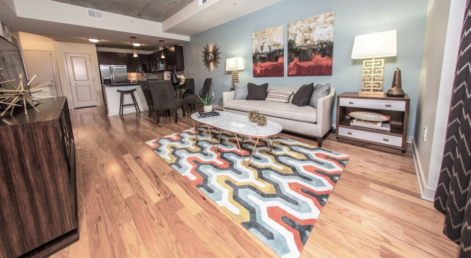 Modern living room with colorful geometric rug, sleek furniture, and open kitchen layout.