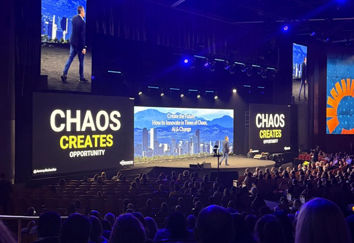 A speaker addresses a large audience on innovation during chaos, with bold visuals emphasizing opportunity.