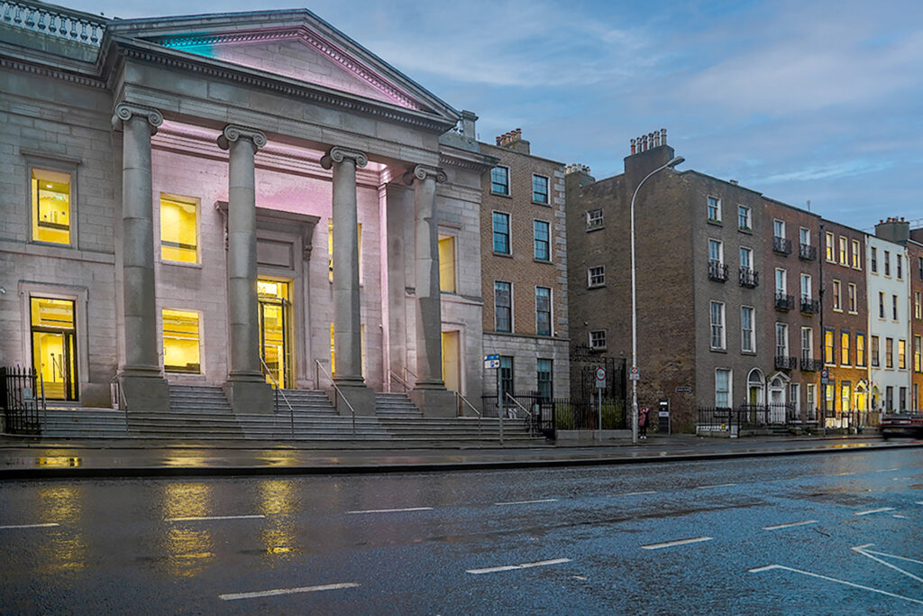 Neoclassical building with columns beside Georgian-style townhouses on a wet city street.