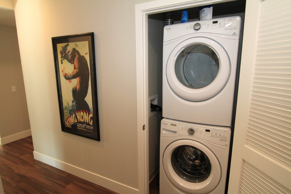 Stacked washer and dryer in a closet beside a framed King Kong poster on a hallway wall.