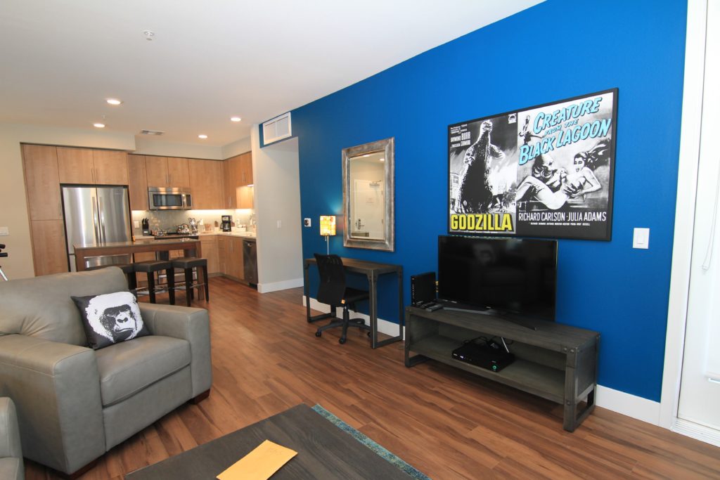 Modern living space with blue accent wall, open kitchen, and retro movie poster decor.