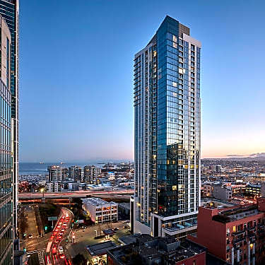 A modern high-rise tower overlooks a bustling urban landscape at dusk, with city lights and traffic.