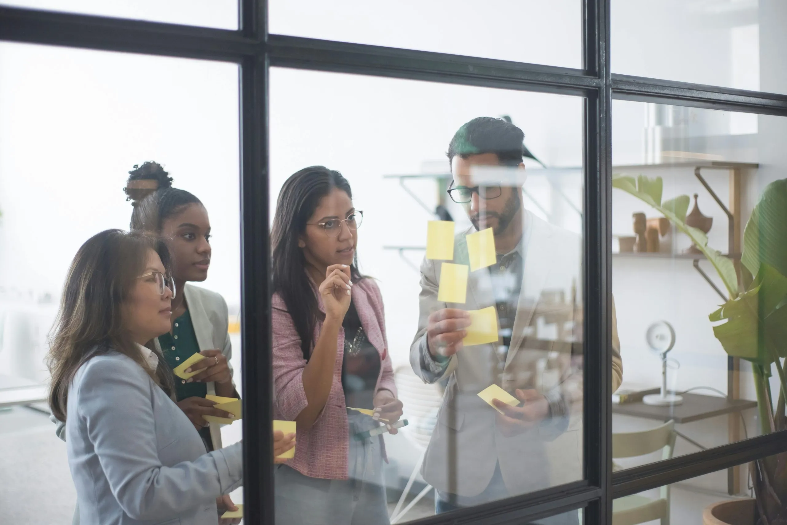 A group collaborates in an office, brainstorming ideas with sticky notes on a glass wall.