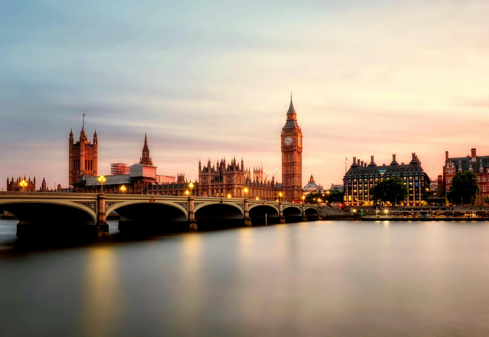 Big Ben and Westminster Bridge at sunset, reflecting on the calm waters of the River Thames.
