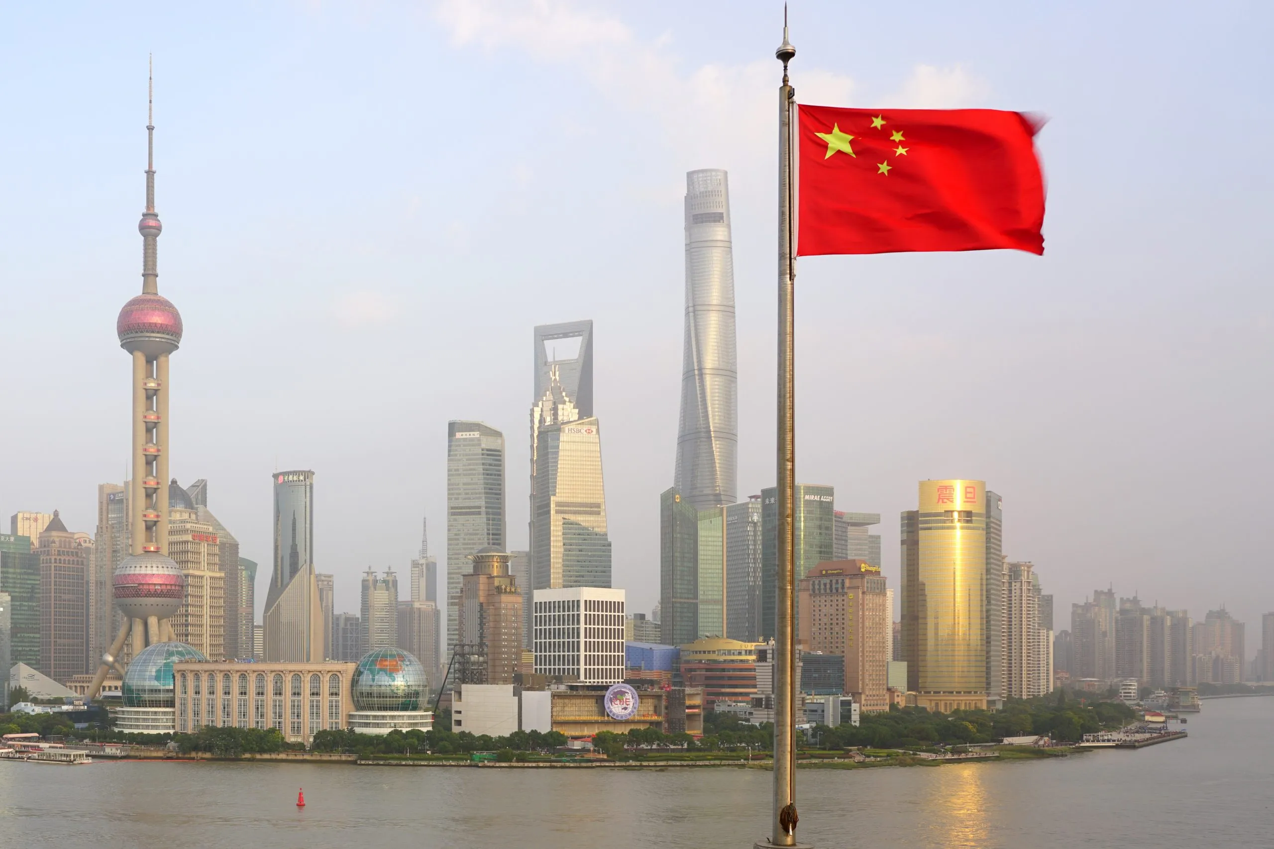 Shanghai skyline with iconic skyscrapers and the Chinese flag prominently displayed in the foreground.