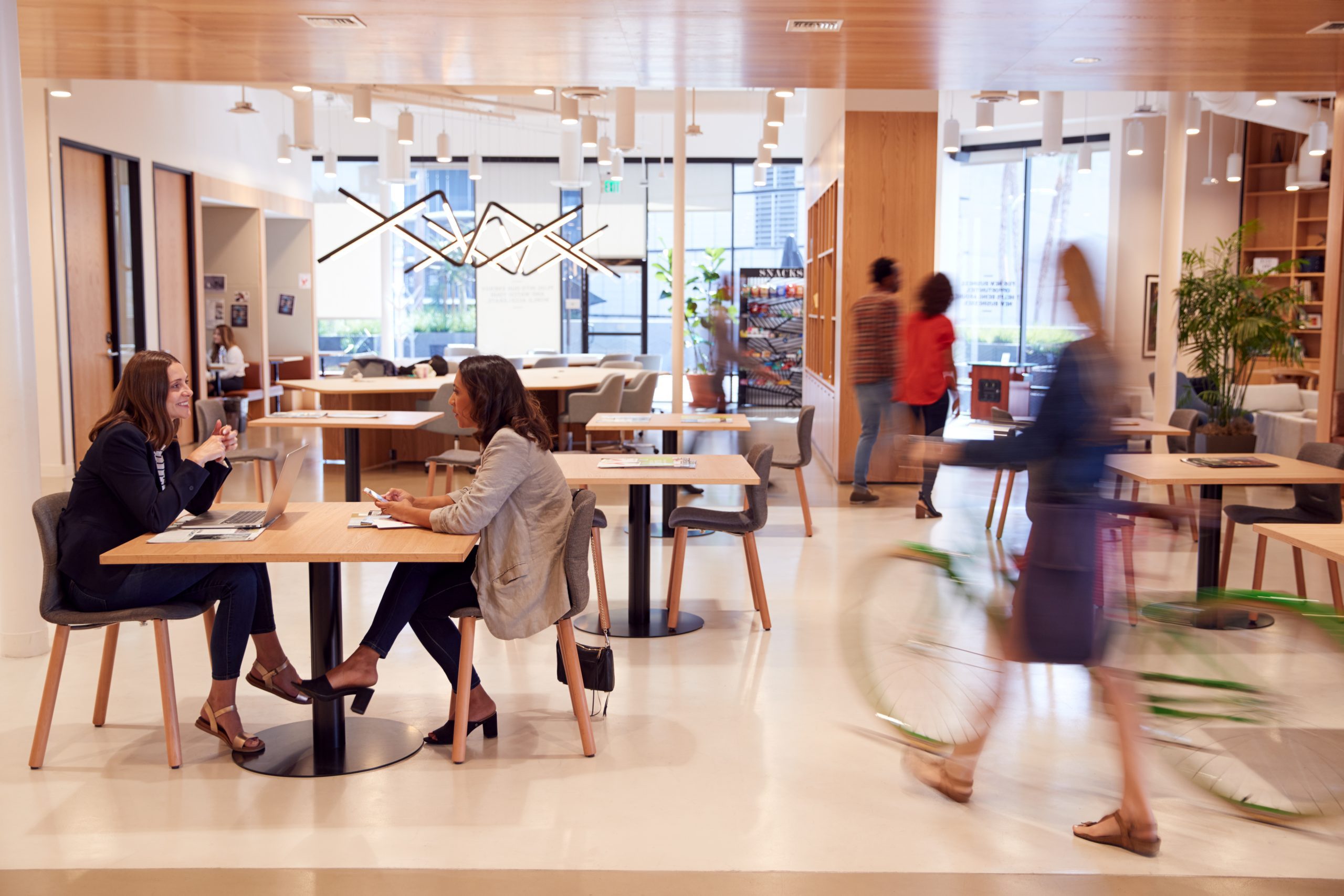 A modern coworking space with people working, walking, and a person riding a bicycle indoors.