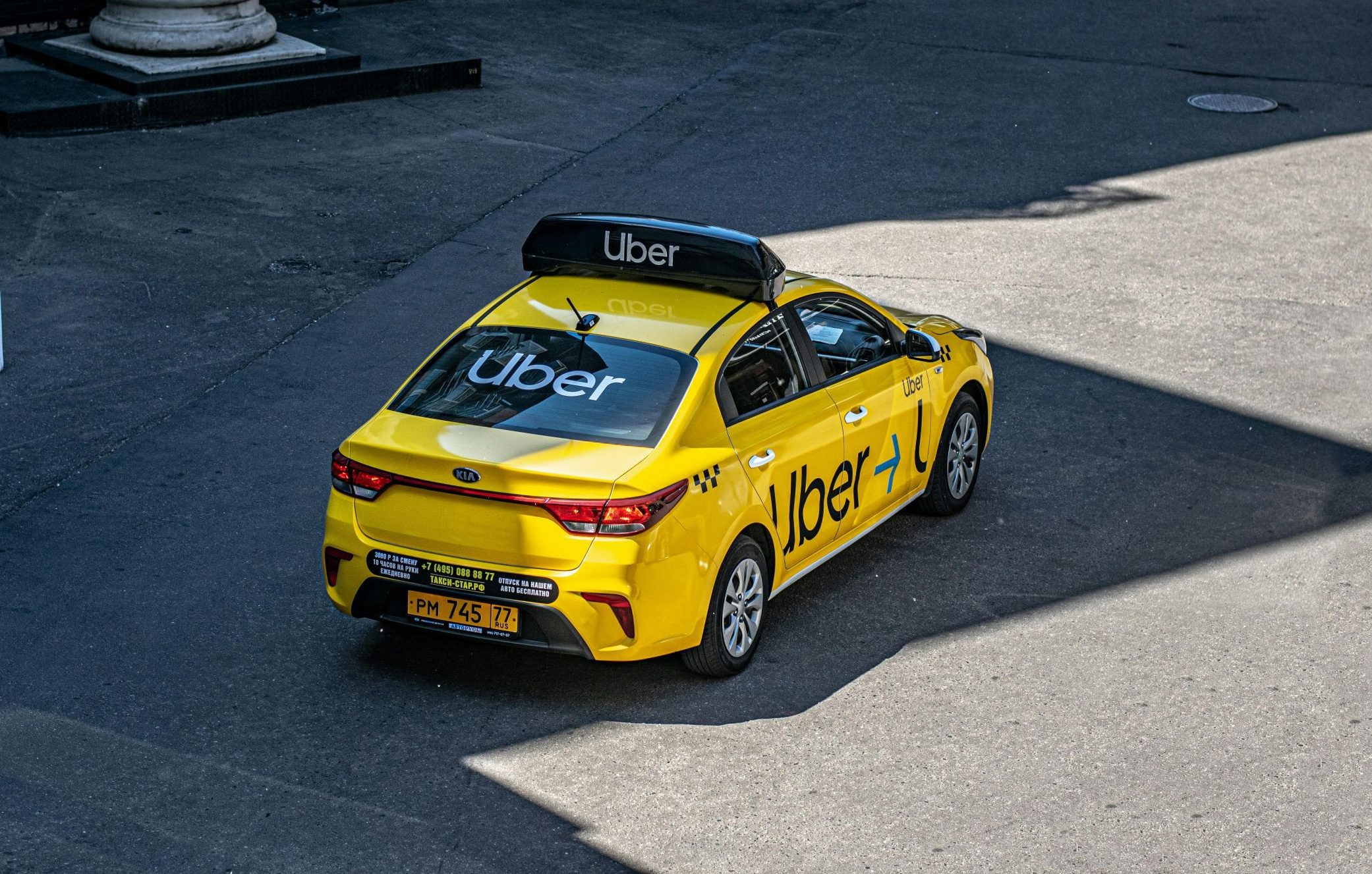 Yellow Kia sedan branded with Uber logos parked on a street under partial sunlight.