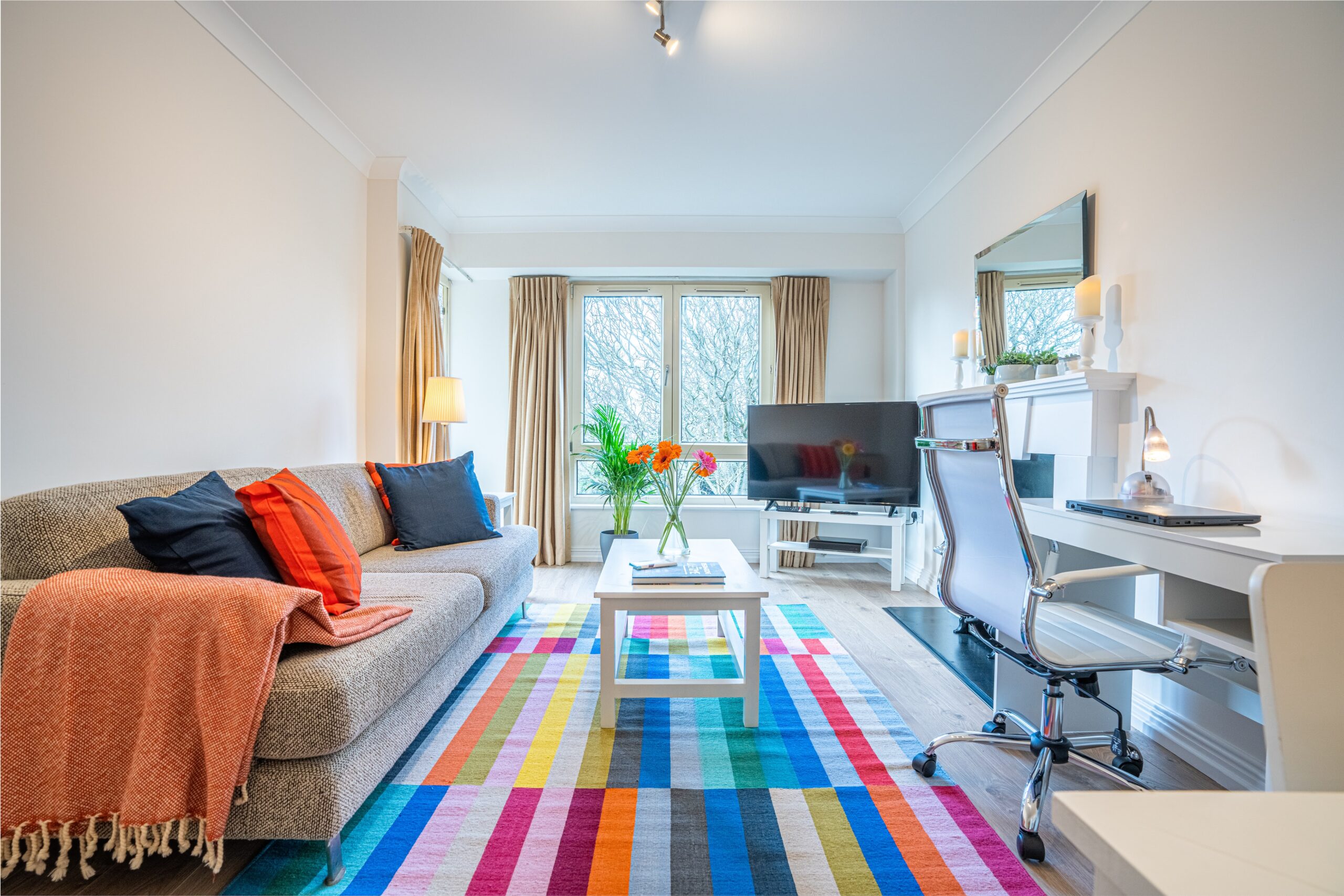Bright living room with modern decor, colorful rug, and a workspace by the window.
